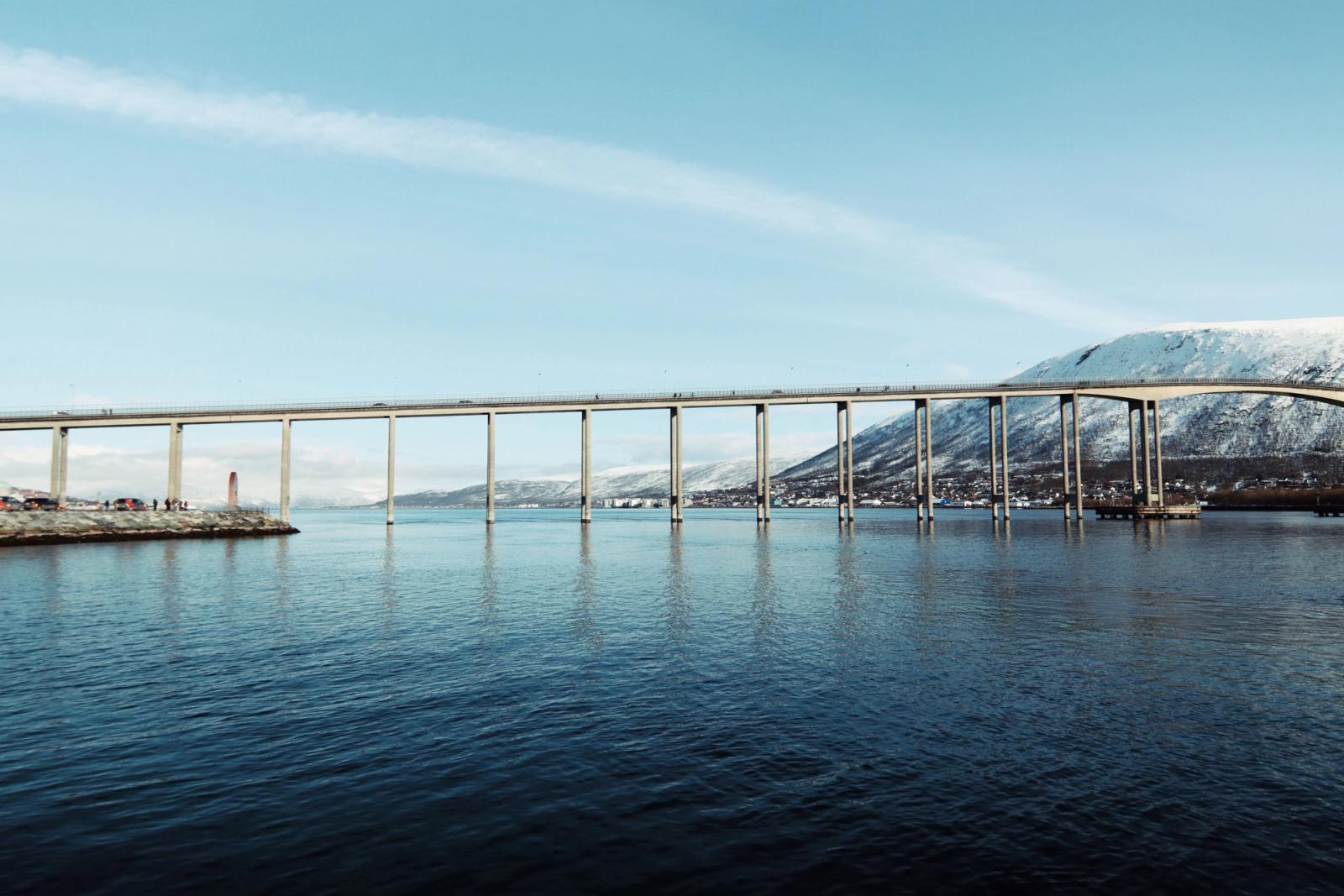 Scenic view of Tromsø Bridge spanning the Arctic waters against a snowy mountain backdrop
