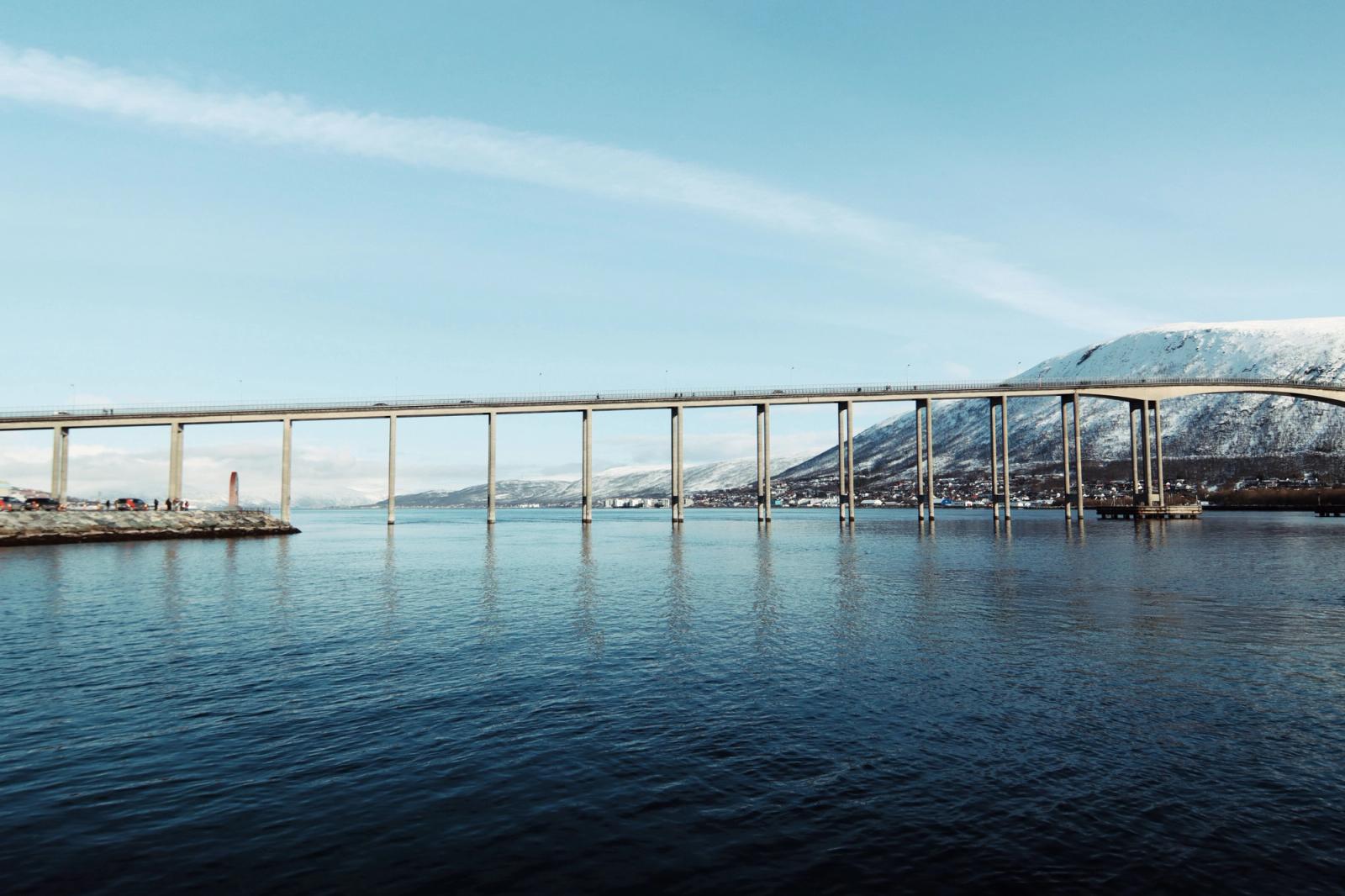 Scenic view of Tromsø Bridge spanning the Arctic waters against a snowy mountain backdrop