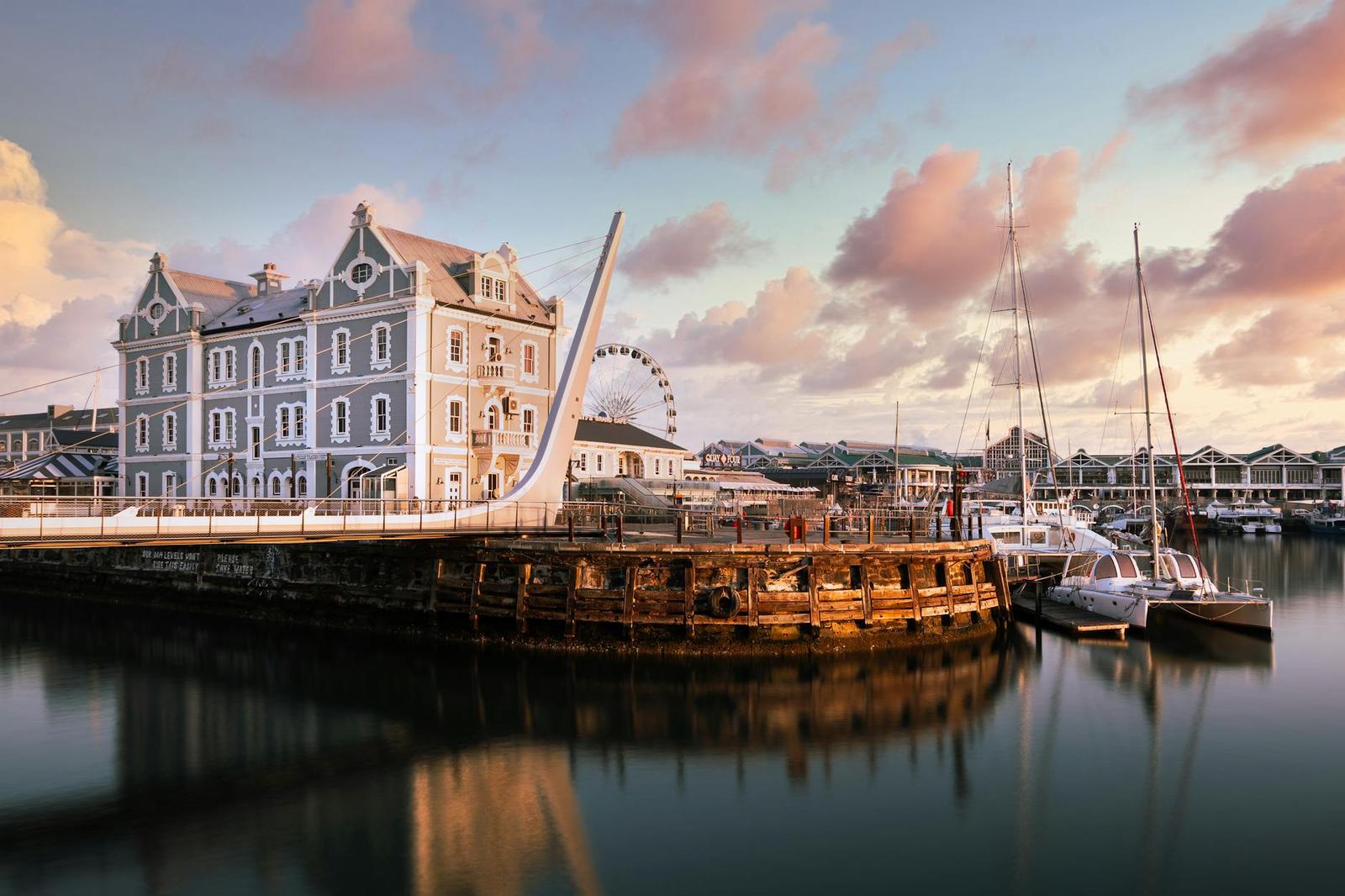 A historic gabled waterfront building beside a ferris wheel and moored yachts at dusk