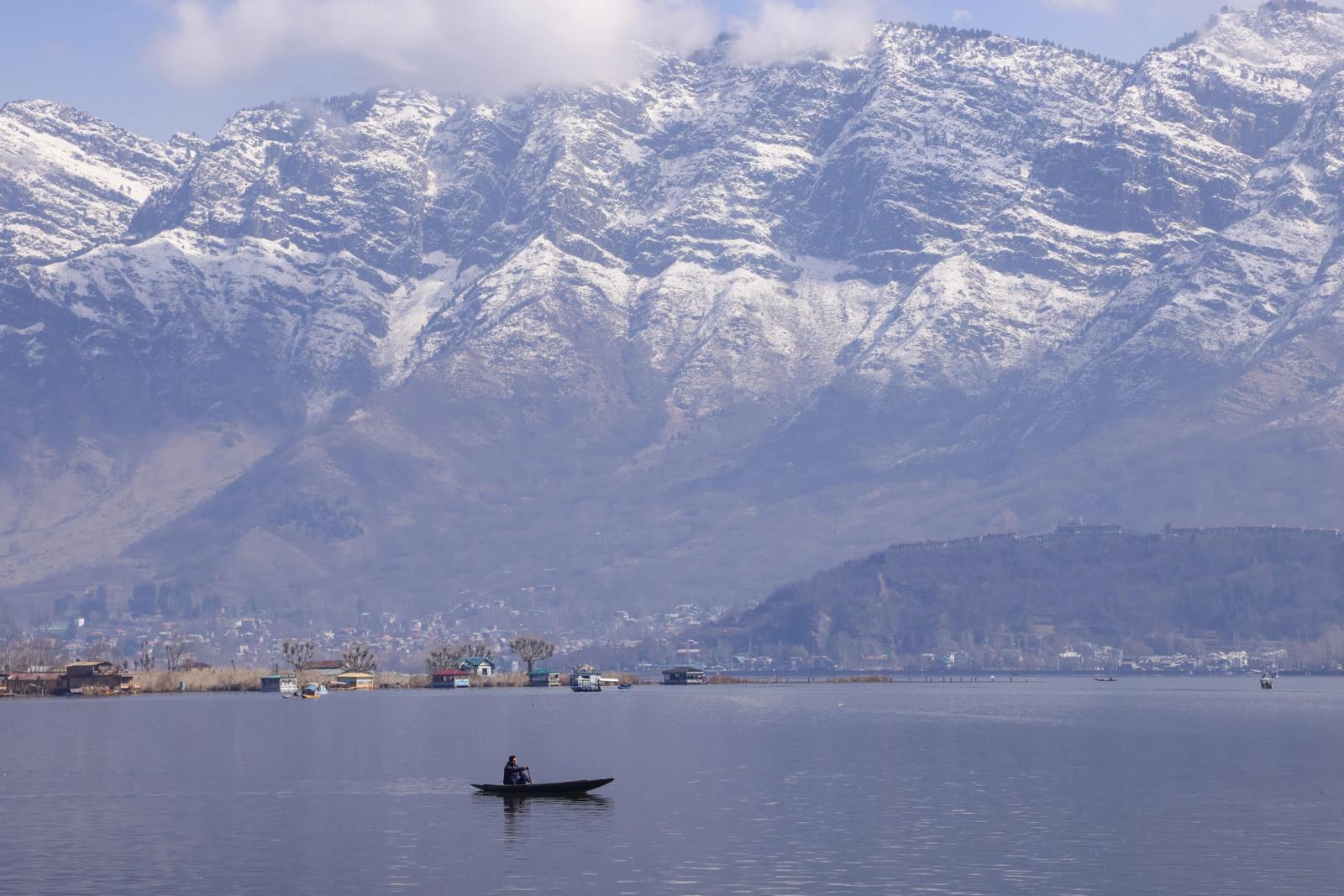 Tranquil scene of a boat on Dal Lake with snow-capped Zabarwan mountains in Srinagar