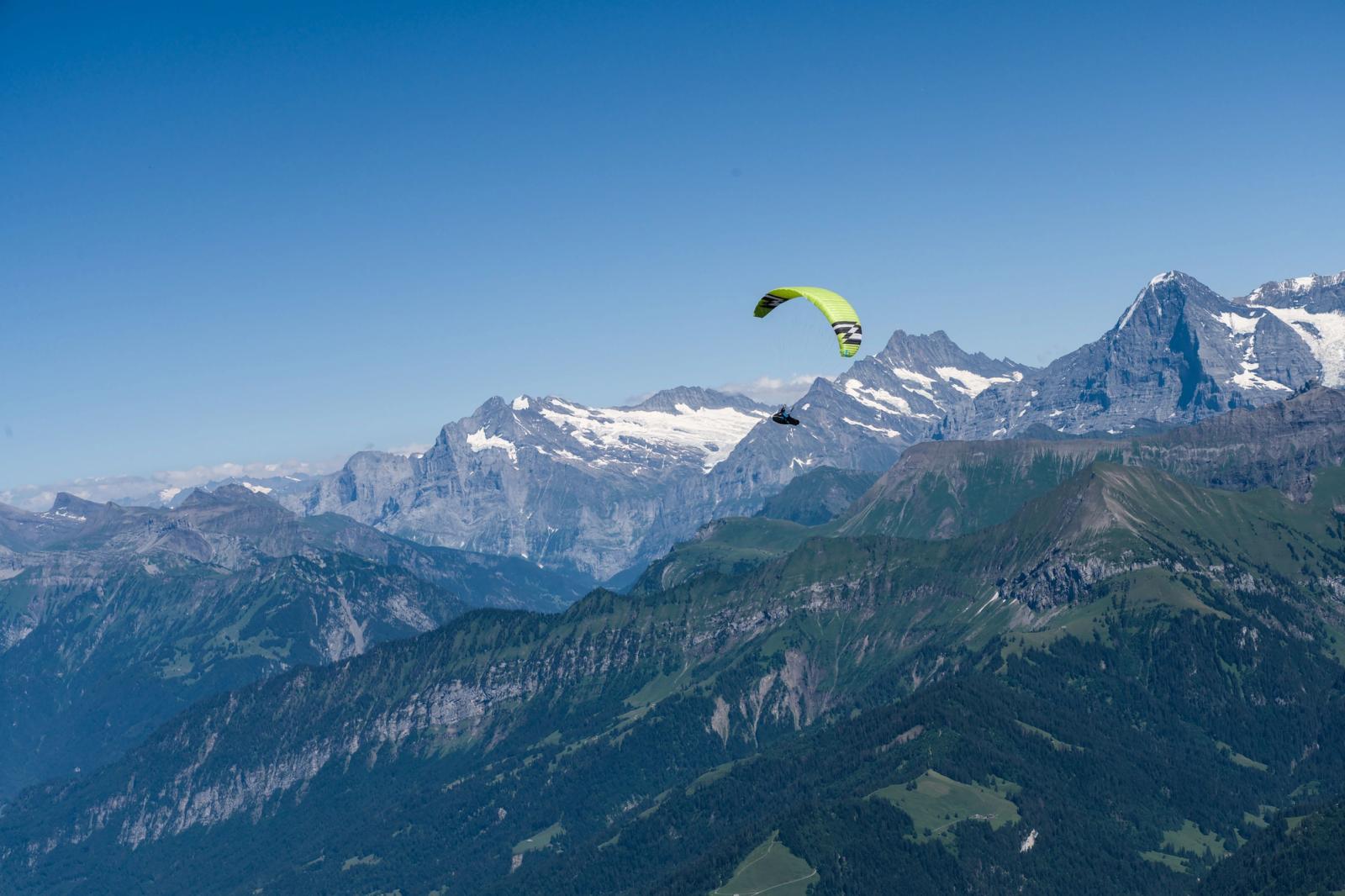 A paraglider soars over the scenic Swiss Alps with clear blue skies in summer