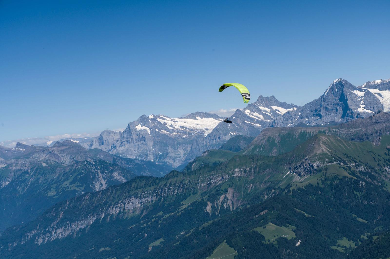A paraglider soars over the scenic Swiss Alps with clear blue skies in summer
