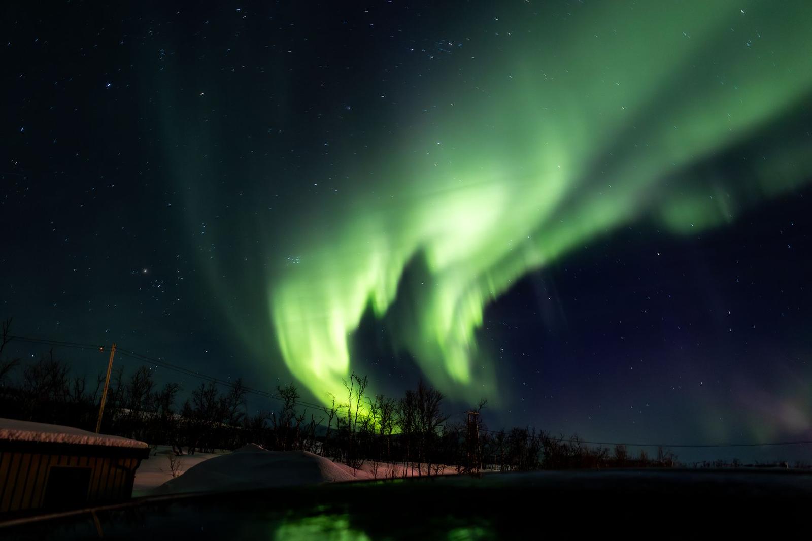 Green aurora glowing above a snow-covered cabin at night