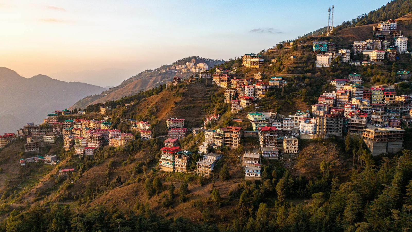 A hill town of scattered houses on a green ridge lit by a hazy sunset