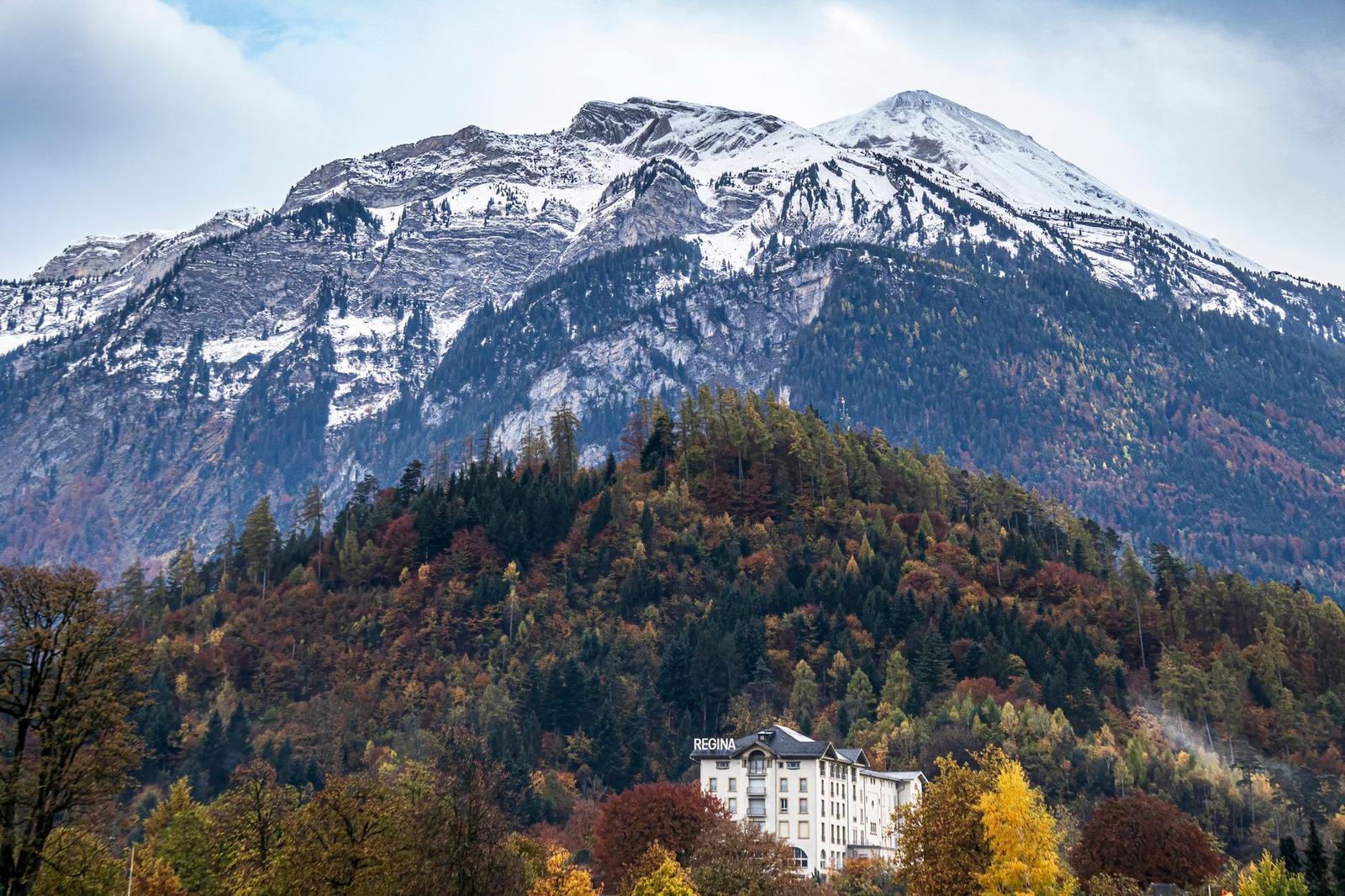 Cream hotel building nestled below a snow-capped mountain and autumn forest