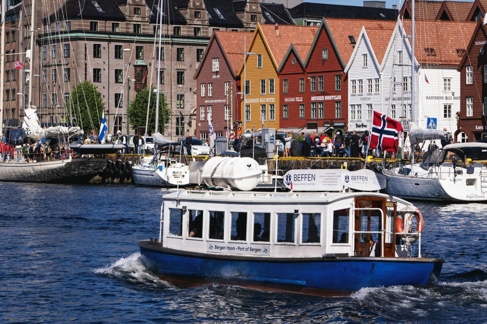 A small passenger boat cruising past colourful gabled wooden buildings on a harbour