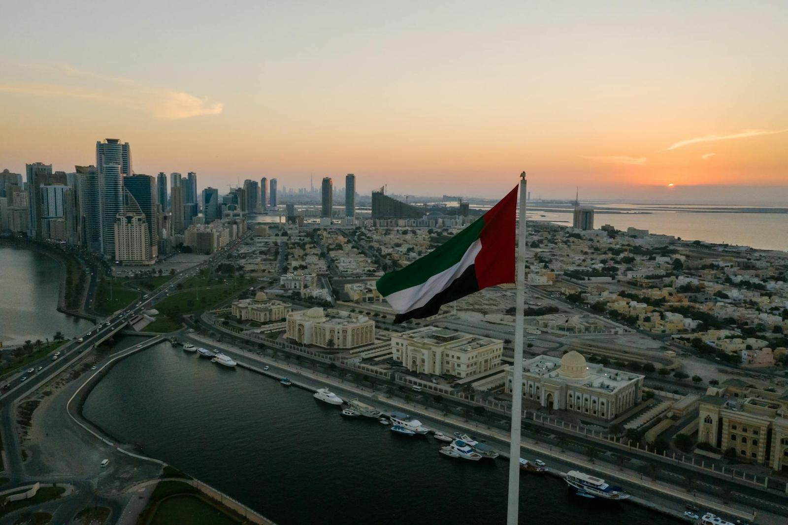A national flag flying over a waterfront city skyline at sunset