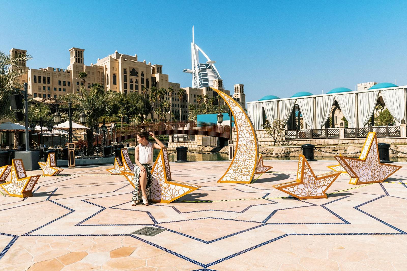A woman relaxes by an artistic installation with the iconic Burj Al Arab in the background