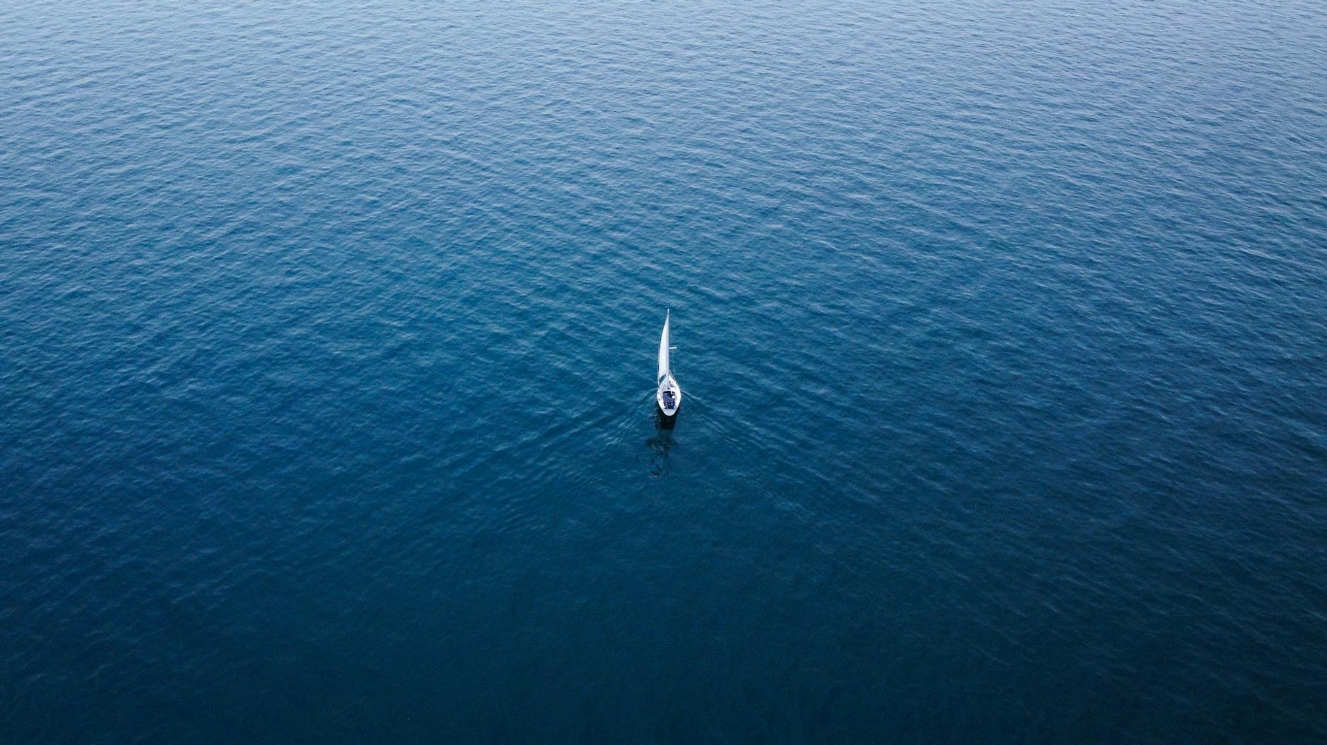 Aerial view of a lone sailboat adrift on deep blue open water