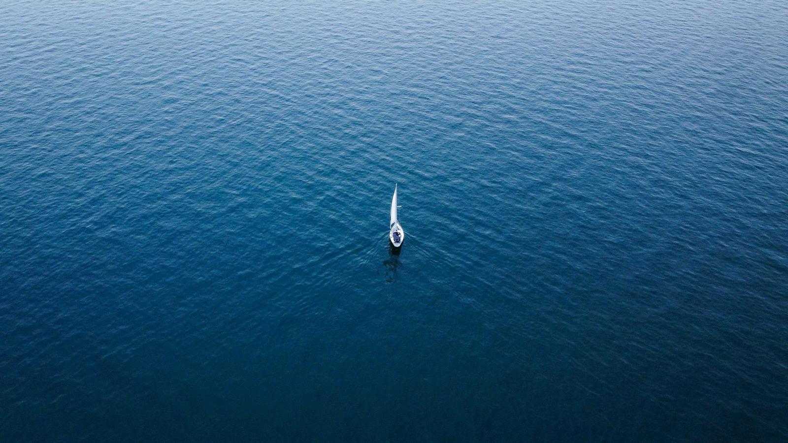 Aerial view of a lone sailboat adrift on deep blue open water