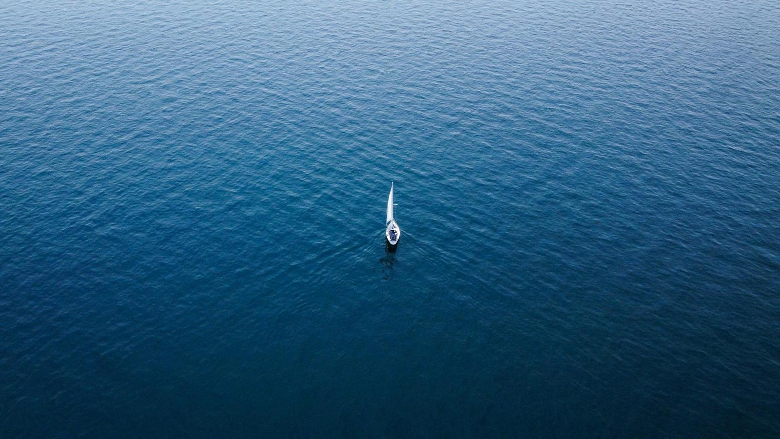 Aerial view of a lone sailboat adrift on deep blue open water