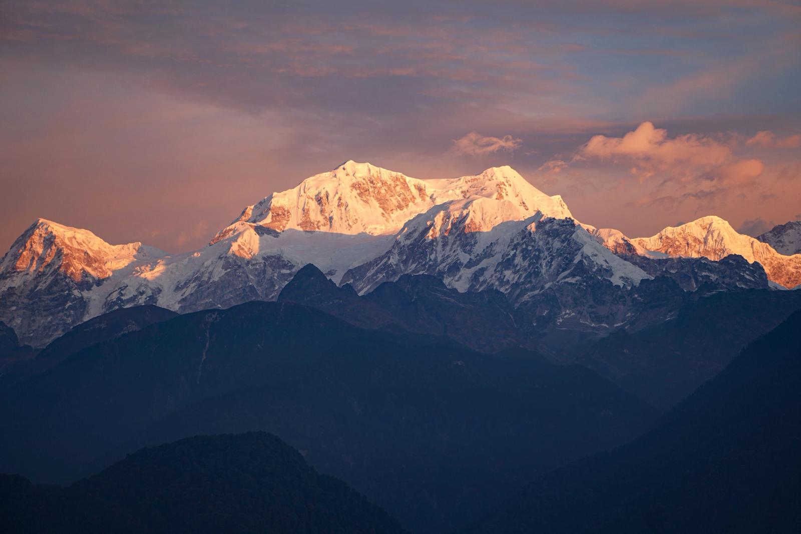 A snow capped mountain range glowing pink at sunset
