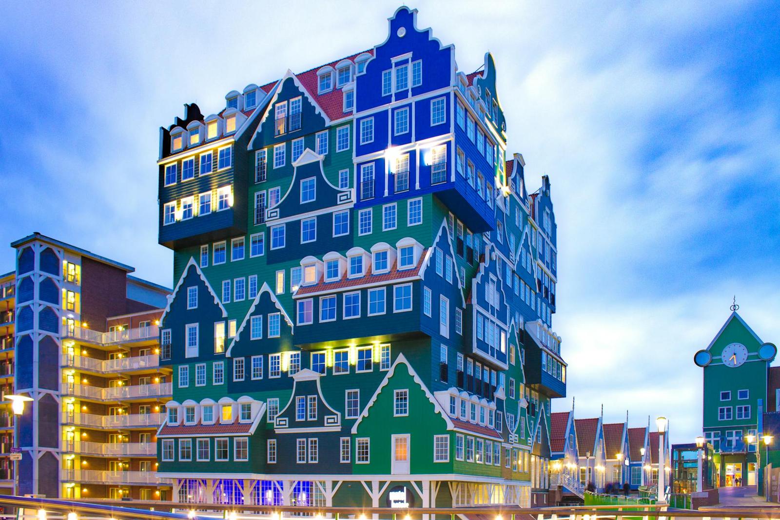 The same stacked gabled-house building lit up at night against a dusky sky