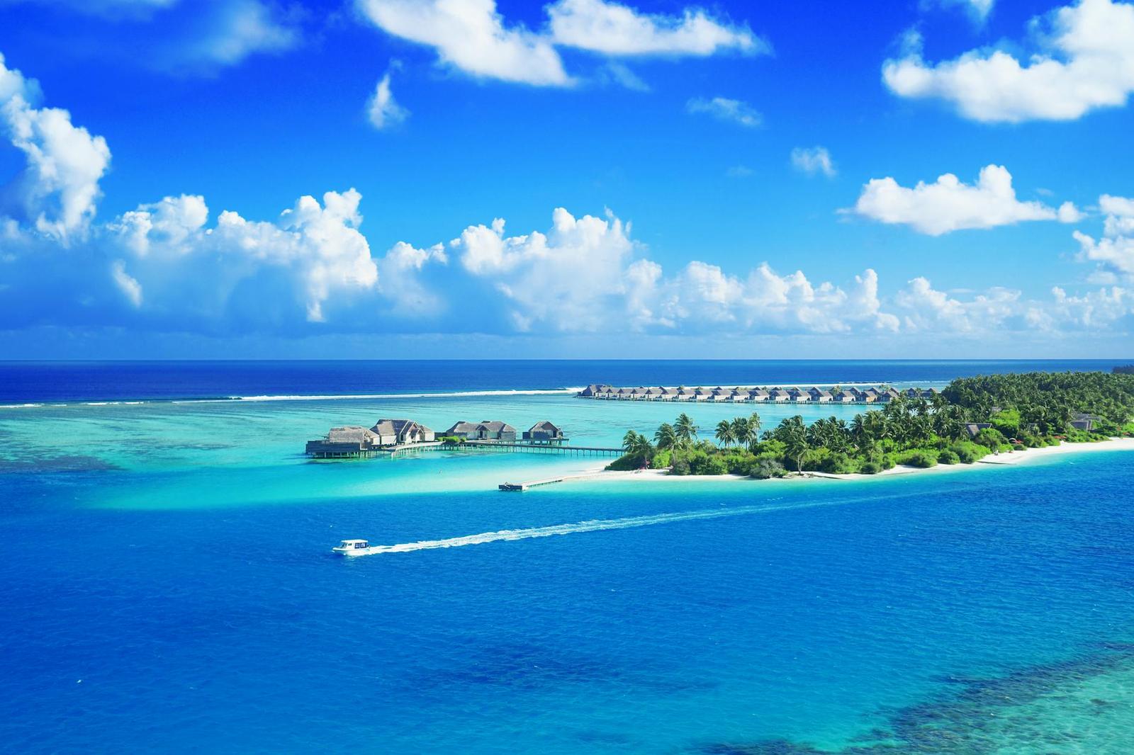A speedboat crossing turquoise water near an overwater villa resort