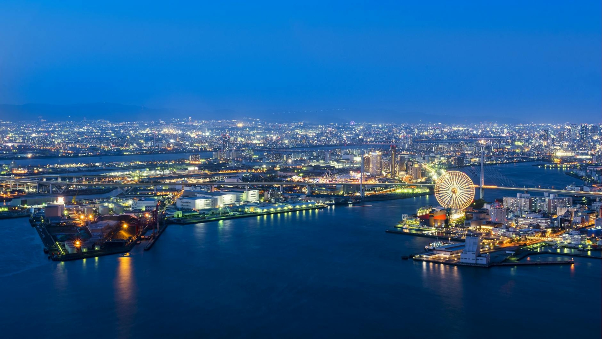 Aerial night view of a harbour city with a lit ferris wheel by the water