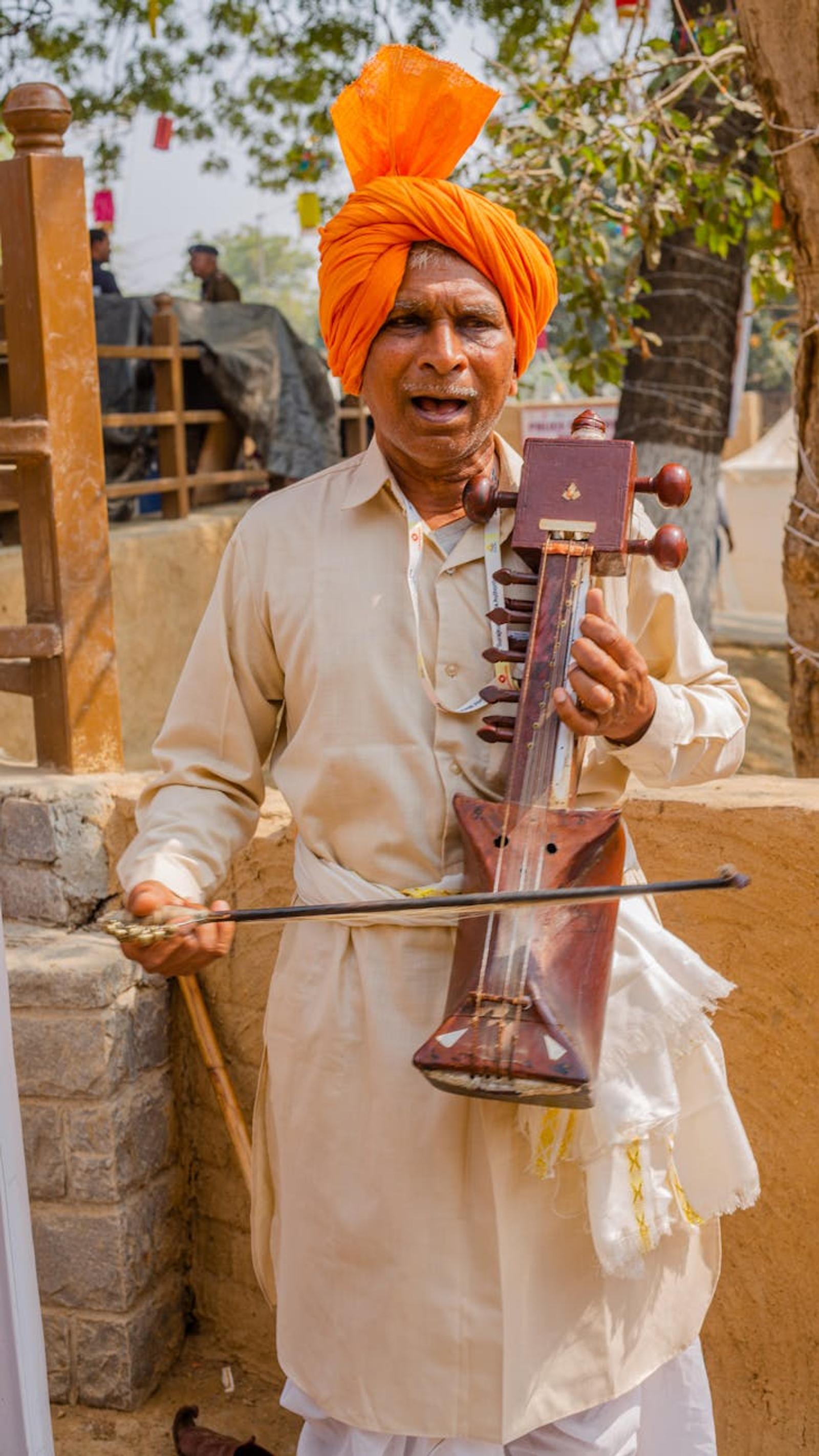 A traditional musician wearing orange turban plays the sarangi outdoors