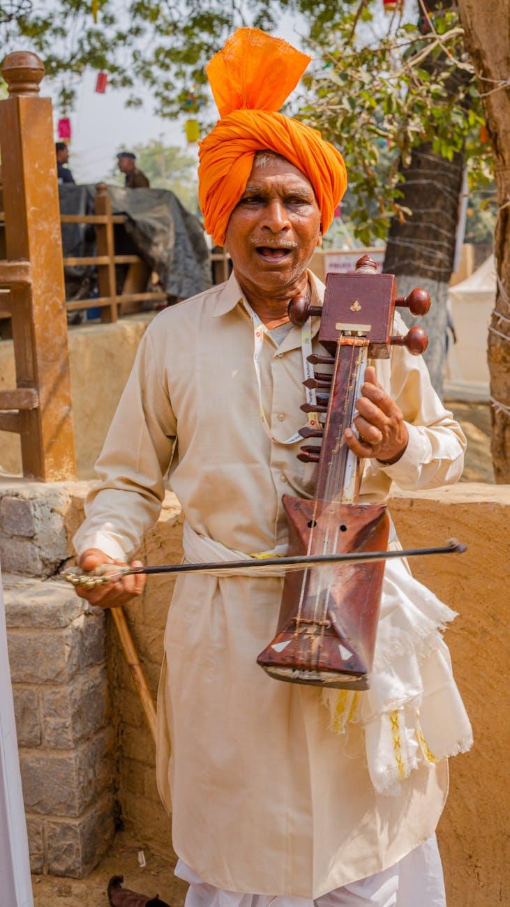 A traditional musician wearing orange turban plays the sarangi outdoors