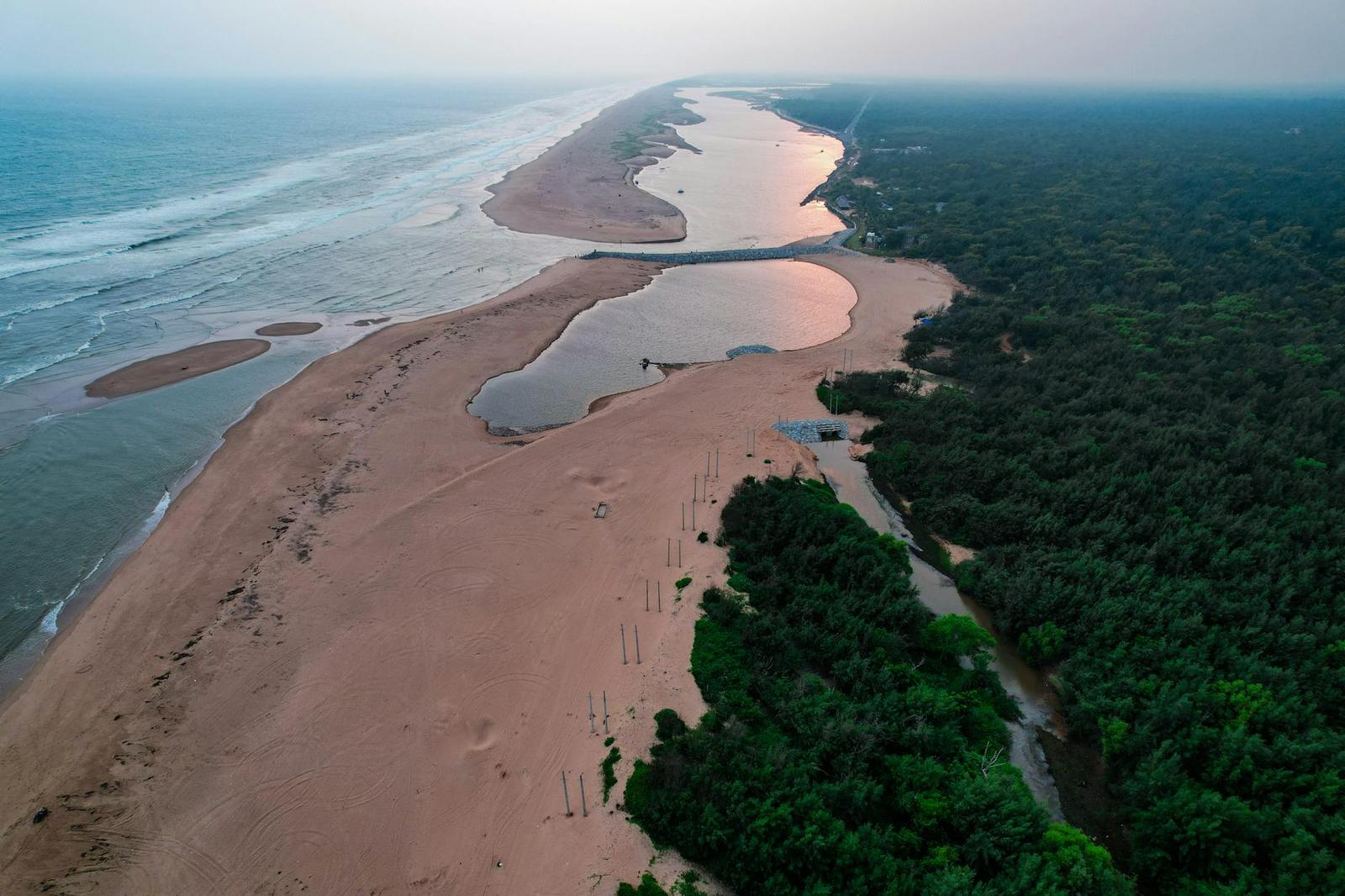 Aerial view of a river mouth winding through coastal dunes at dusk