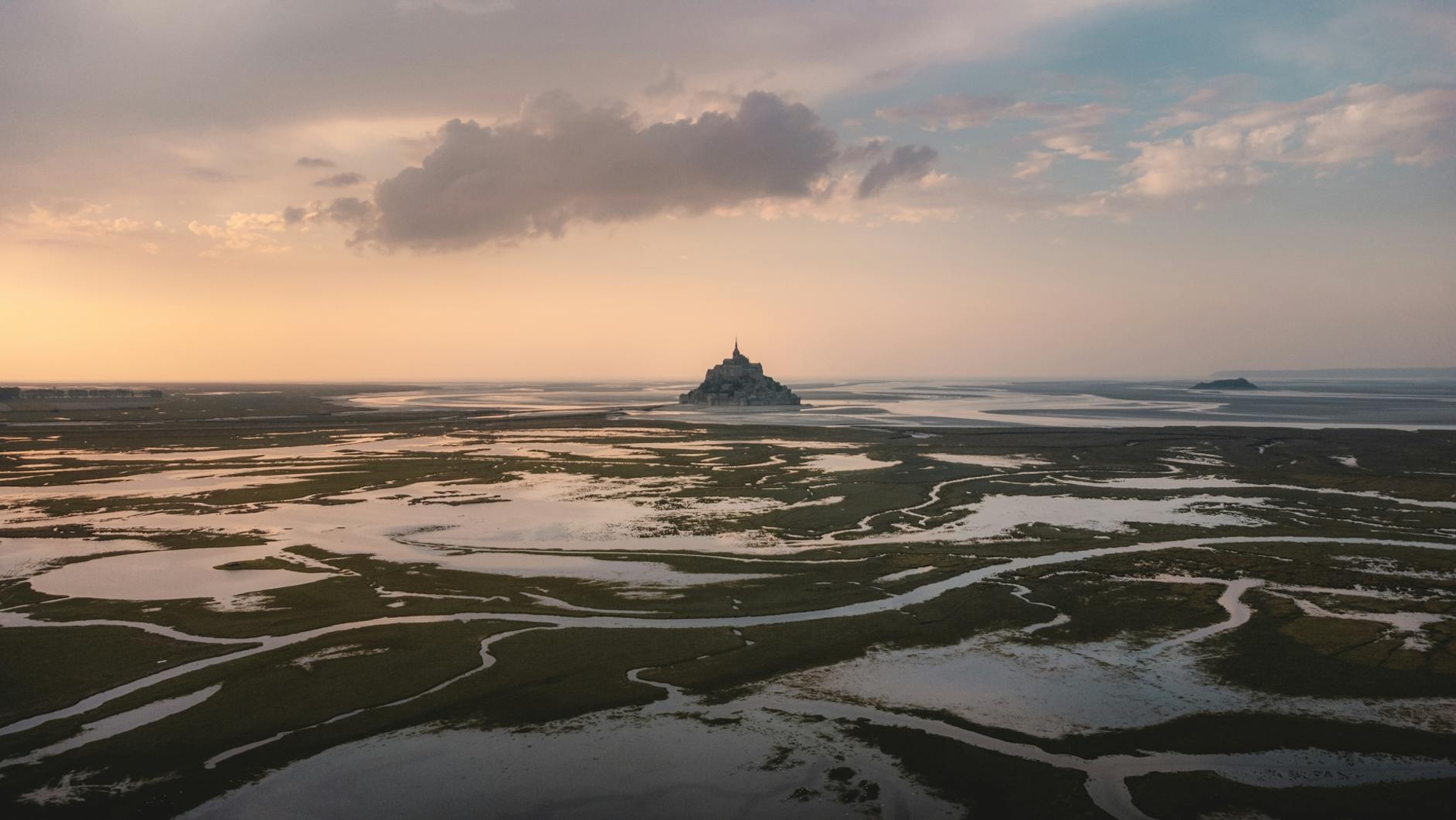 Rocky tidal island abbey rising from wet sand flats at dusk