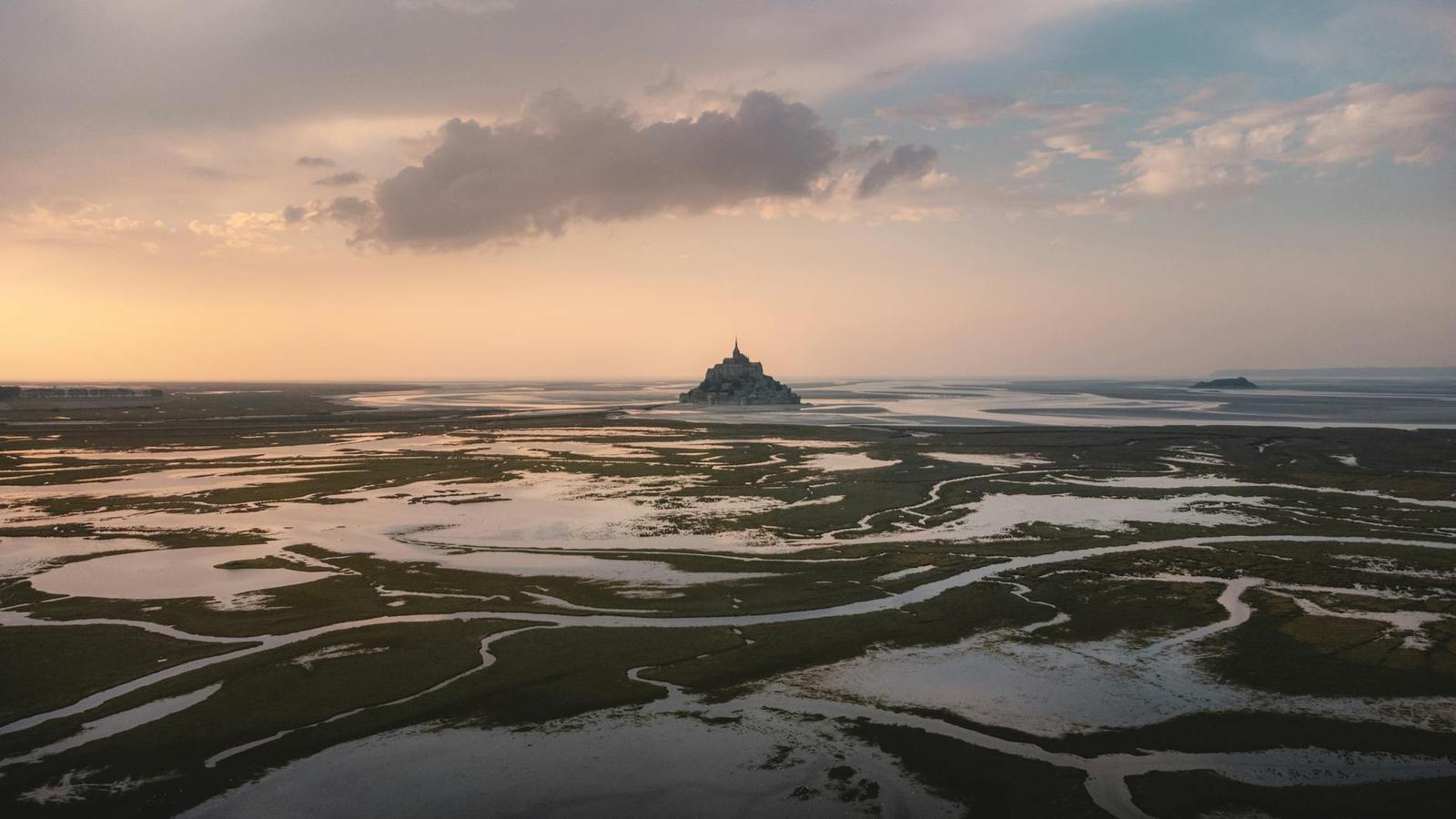 Rocky tidal island abbey rising from wet sand flats at dusk