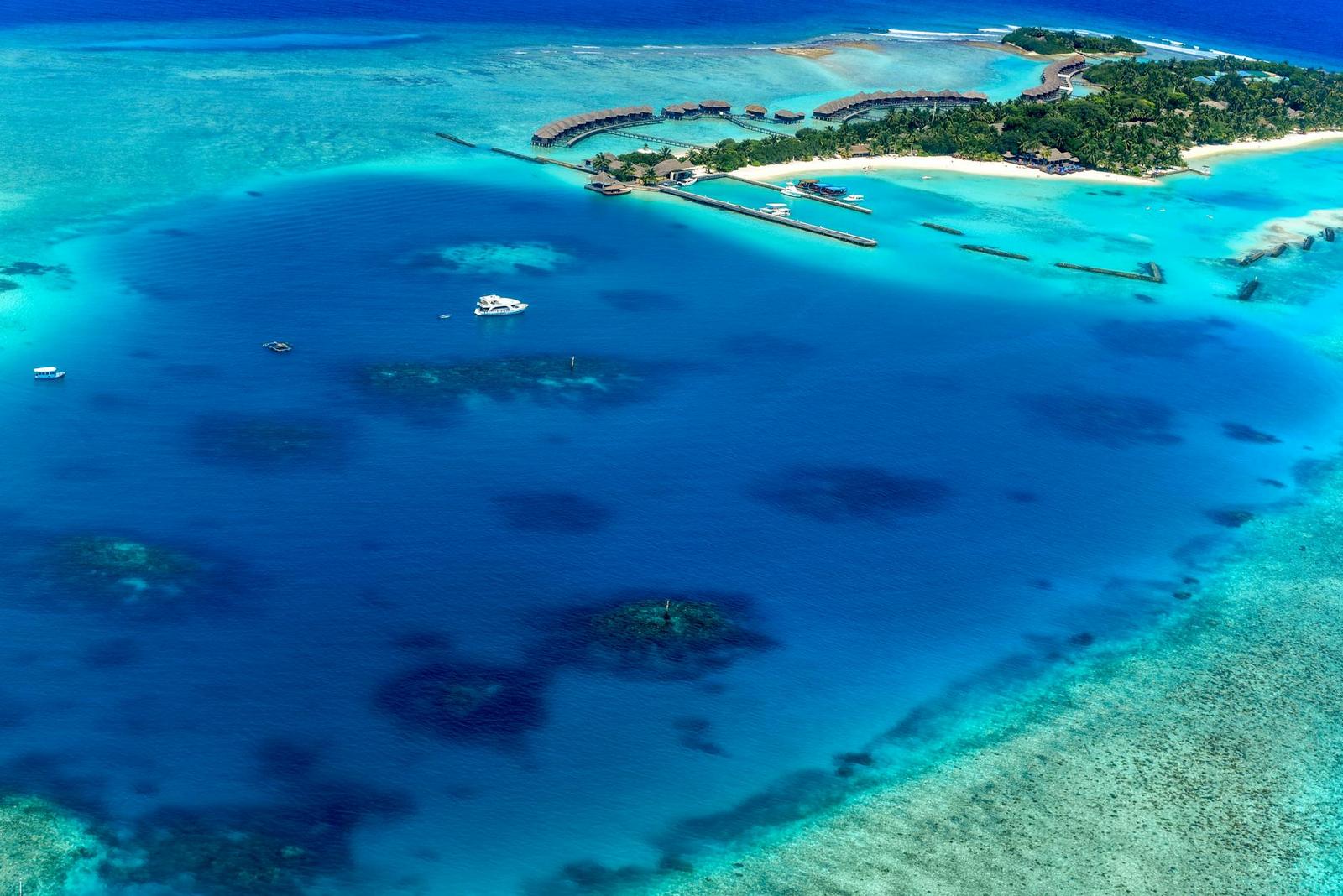 Aerial view of overwater villas bordering a reef dotted lagoon