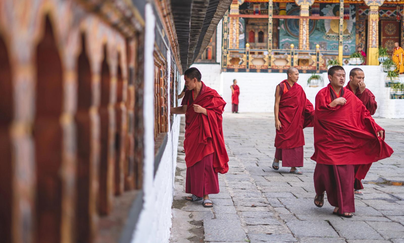 Buddhist monks in red robes walking and interacting in a Bhutan temple courtyard