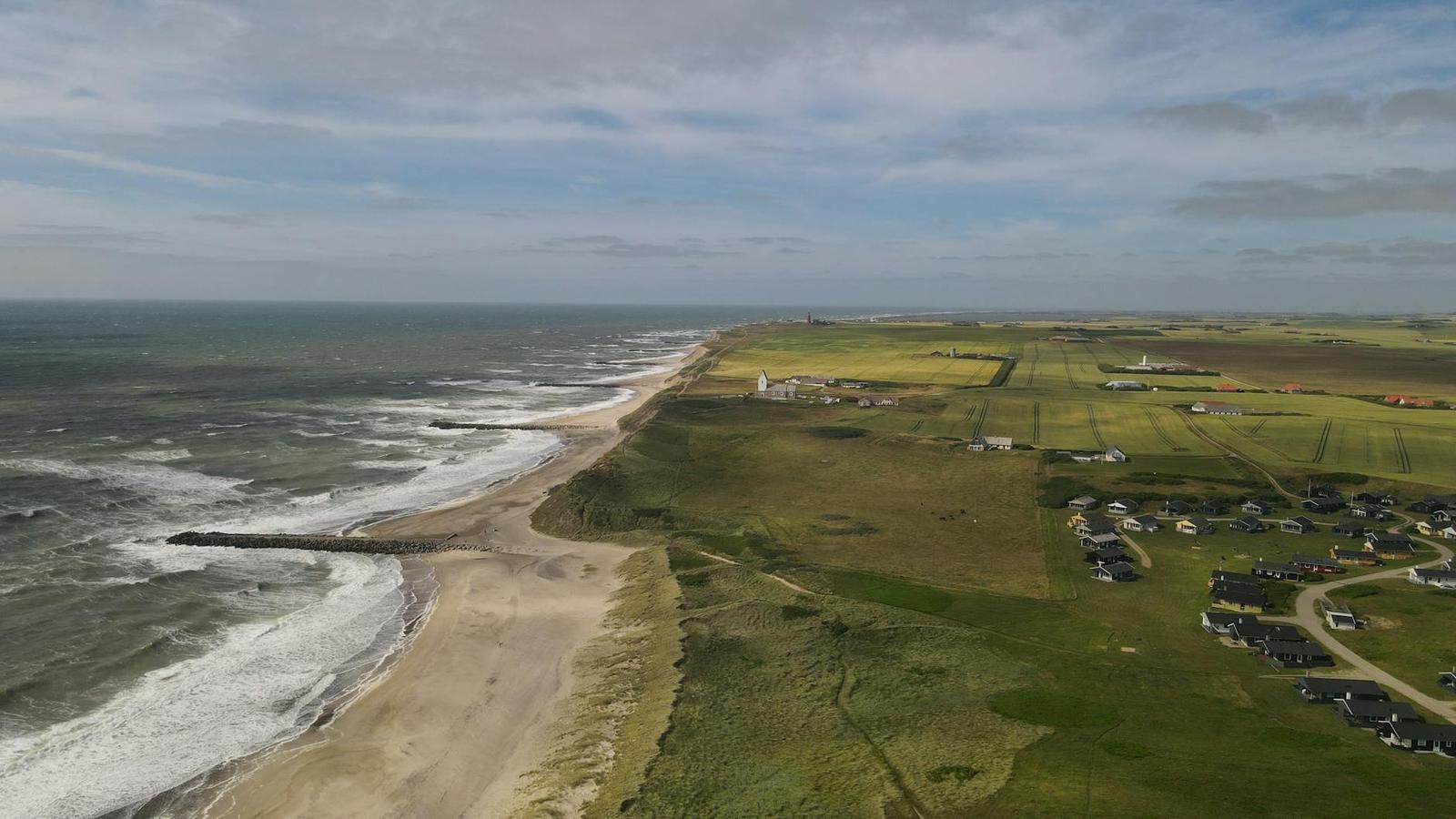 Aerial view of a wave-lined sandy coast bordering green farmland and a village