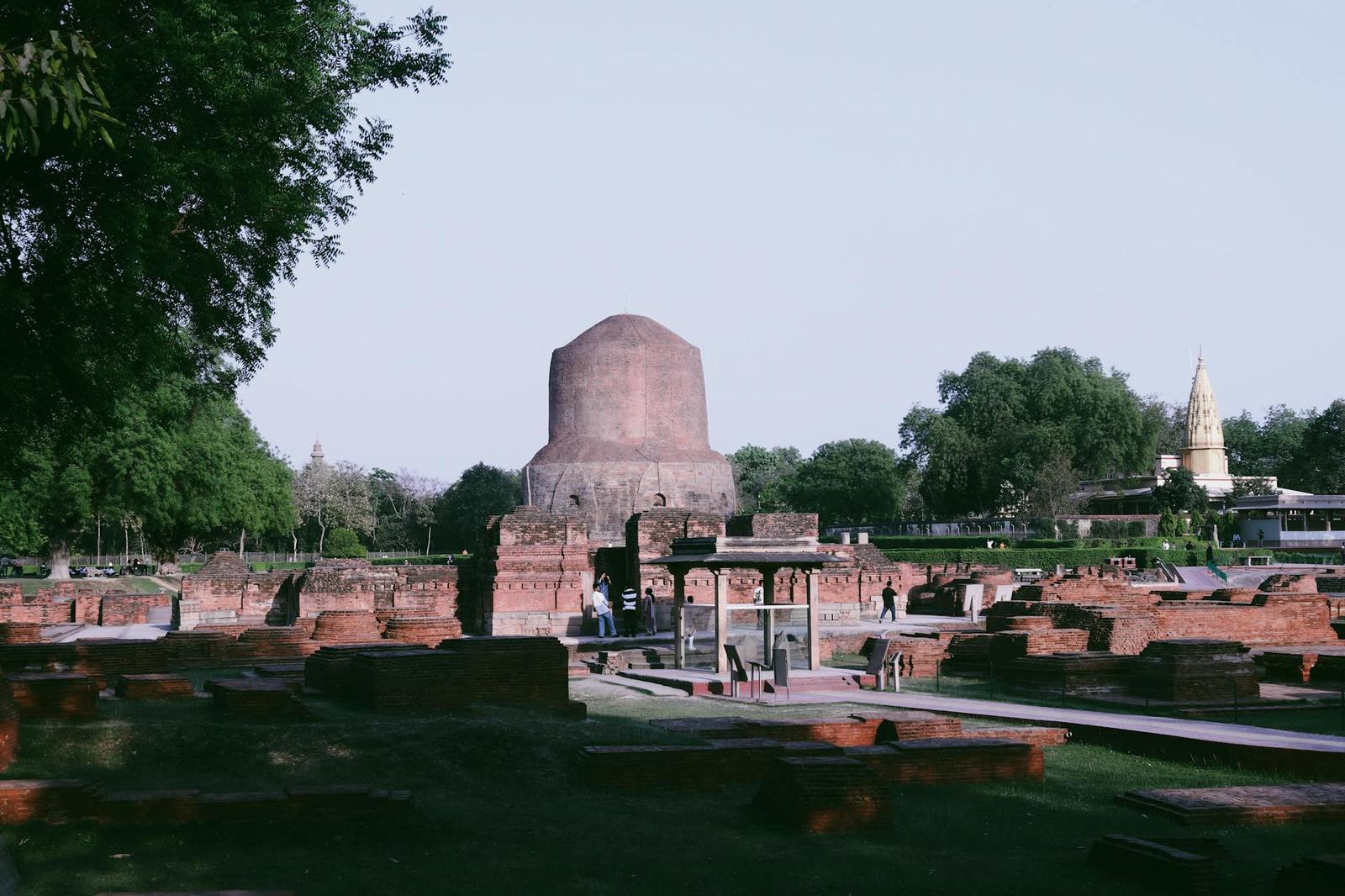 A weathered brick stupa surrounded by ancient ruins with visitors exploring the site