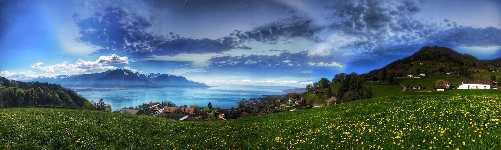 Stunning panoramic view of the Swiss countryside with Lake Geneva and alpine mountains under a vibrant blue sky