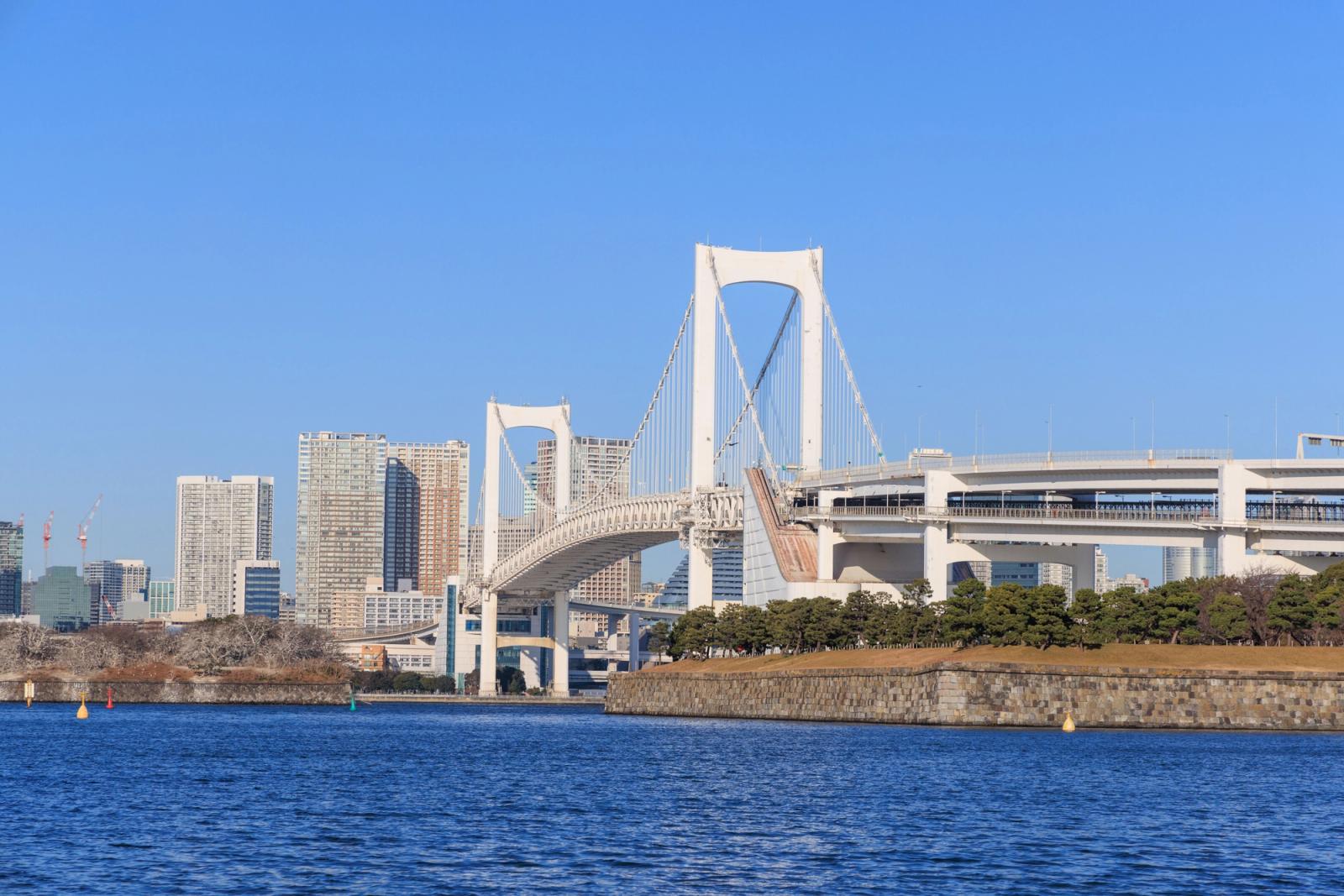 View of the Rainbow Bridge and Tokyo skyline on a bright day, highlighting architectural beauty