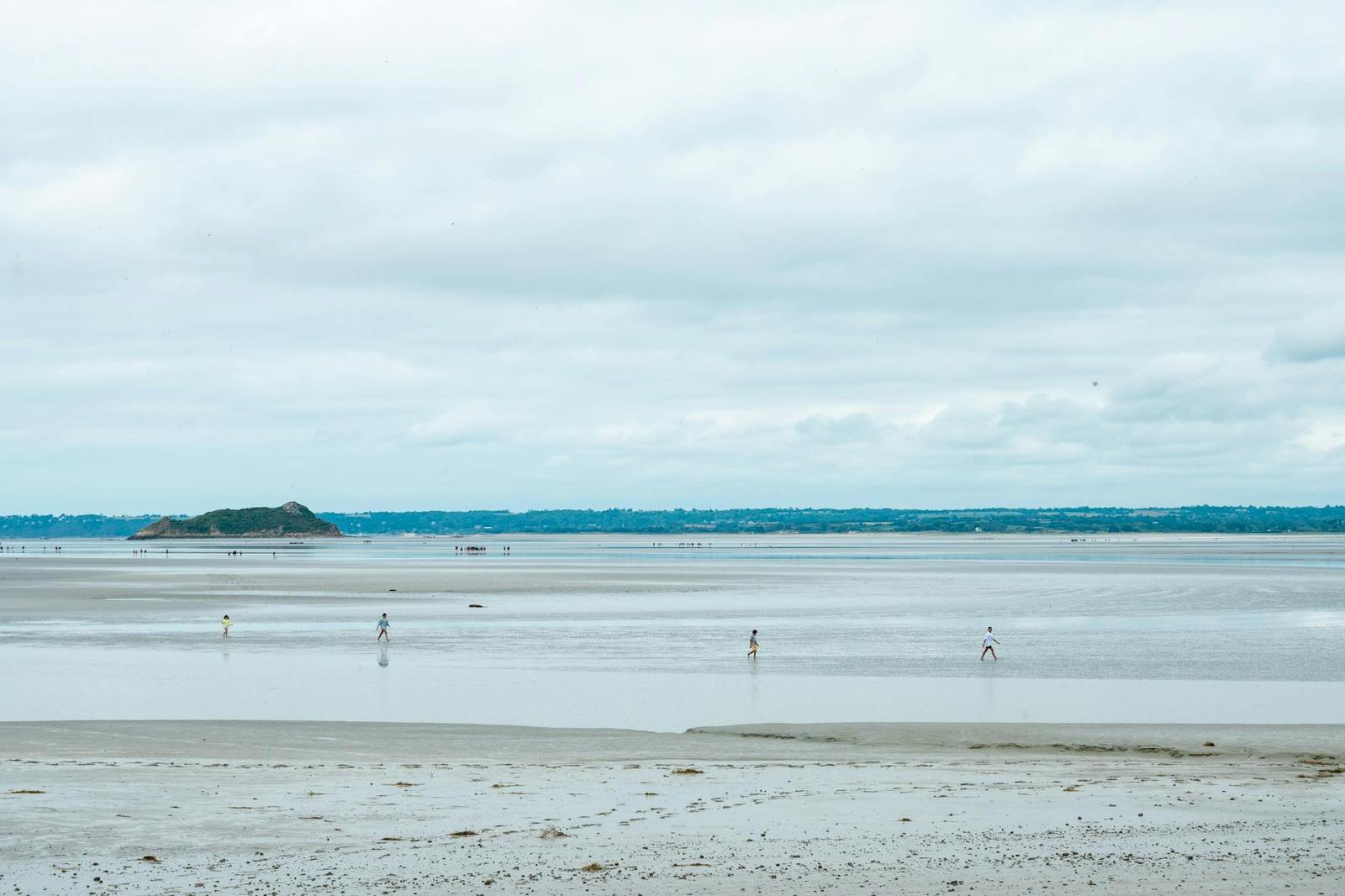 People walking across a wide tidal flat under a cloudy sky