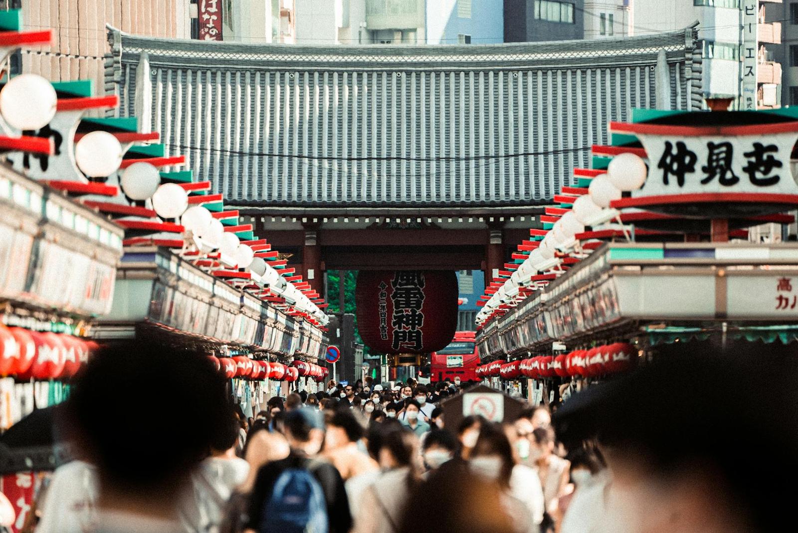 Crowds walking beneath red lanterns toward a grand temple gate
