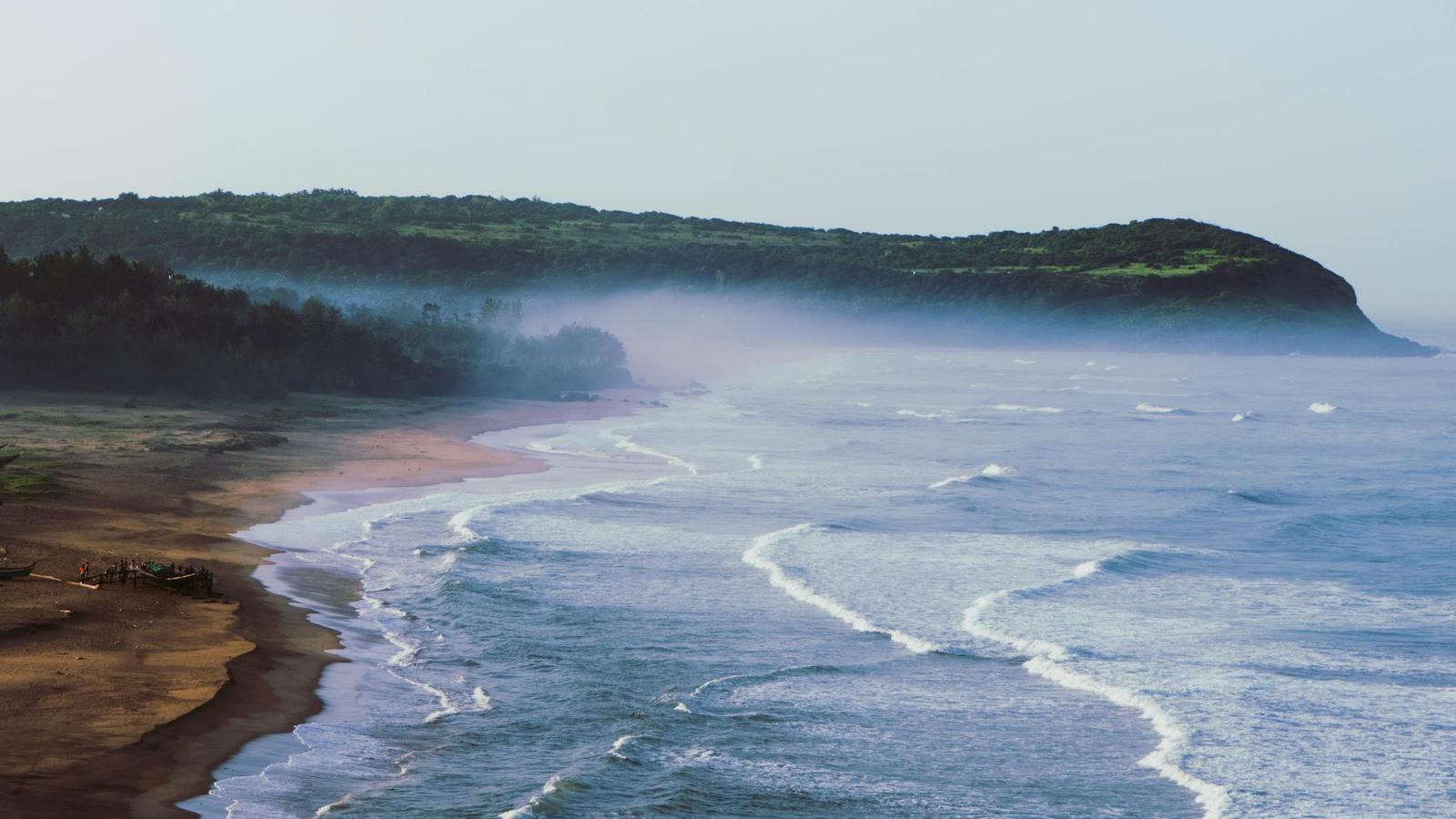 Aerial view of mist drifting over a green headland along a wave lined coast