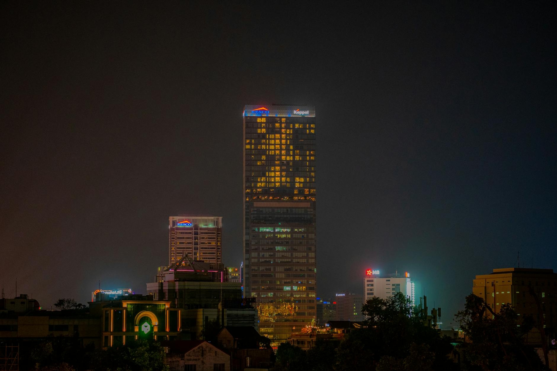 A lit high-rise tower standing above a dark city skyline at night