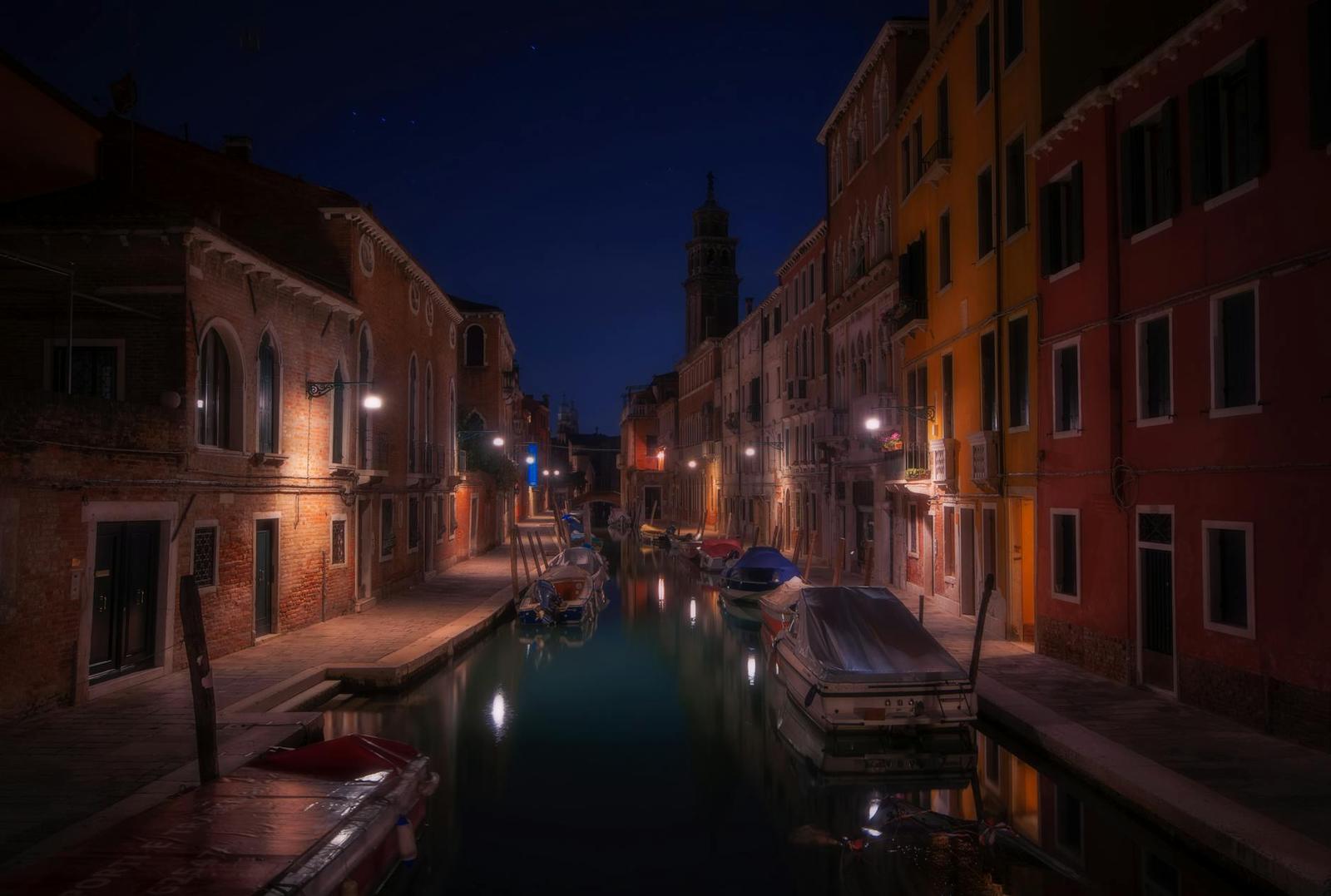 A quiet nighttime canal lined with lamplit buildings and moored boats