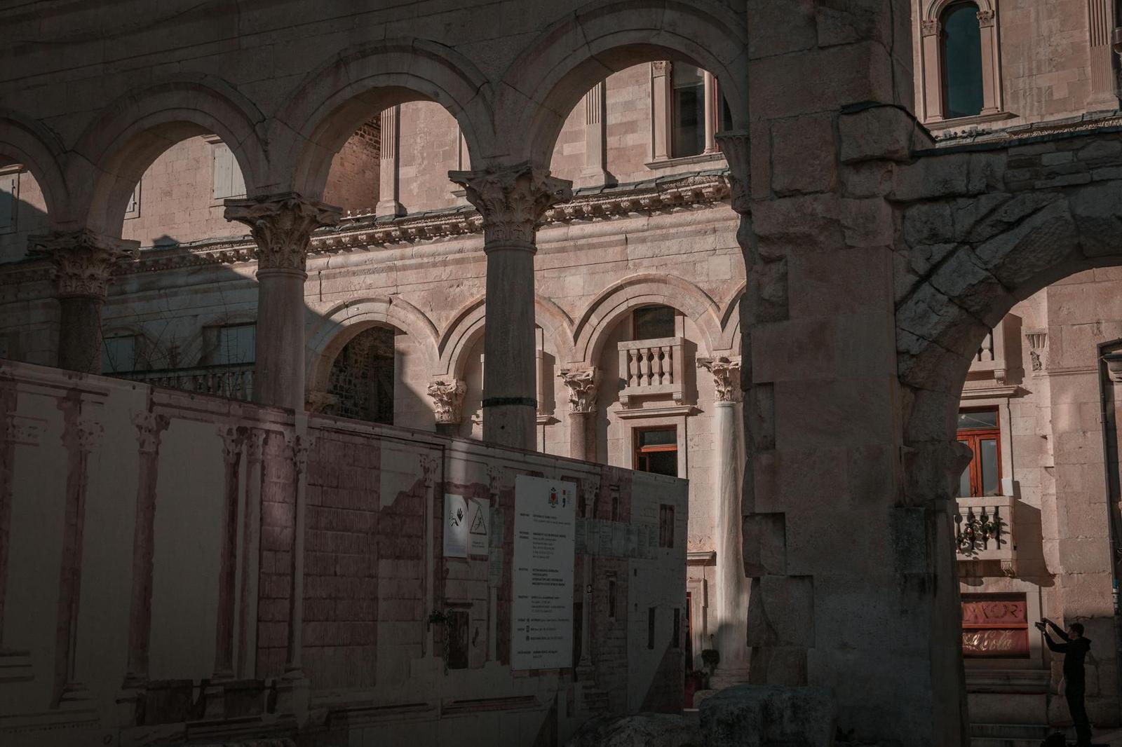 Sunlit stone archways and columns in an ancient courtyard with a lone figure