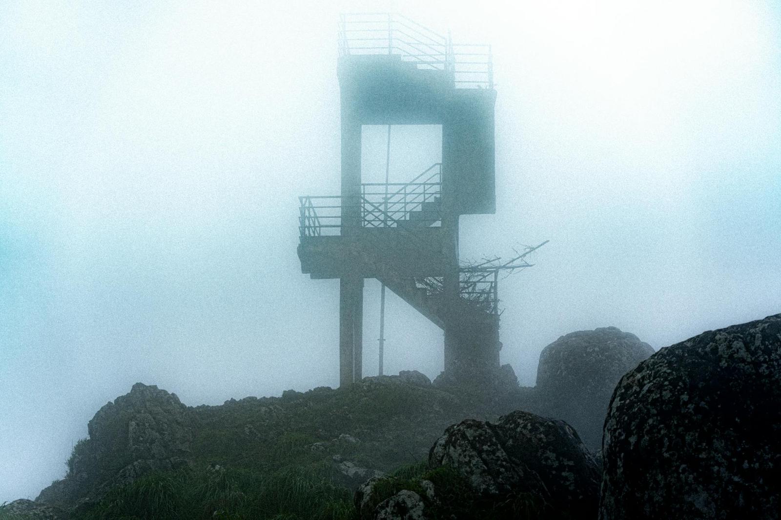 A metal viewing tower shrouded in thick mountain fog