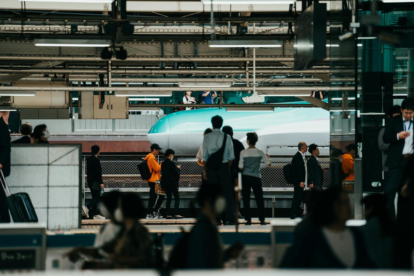 Crowd of people waiting at a bustling Japanese train station with a shinkansen passing