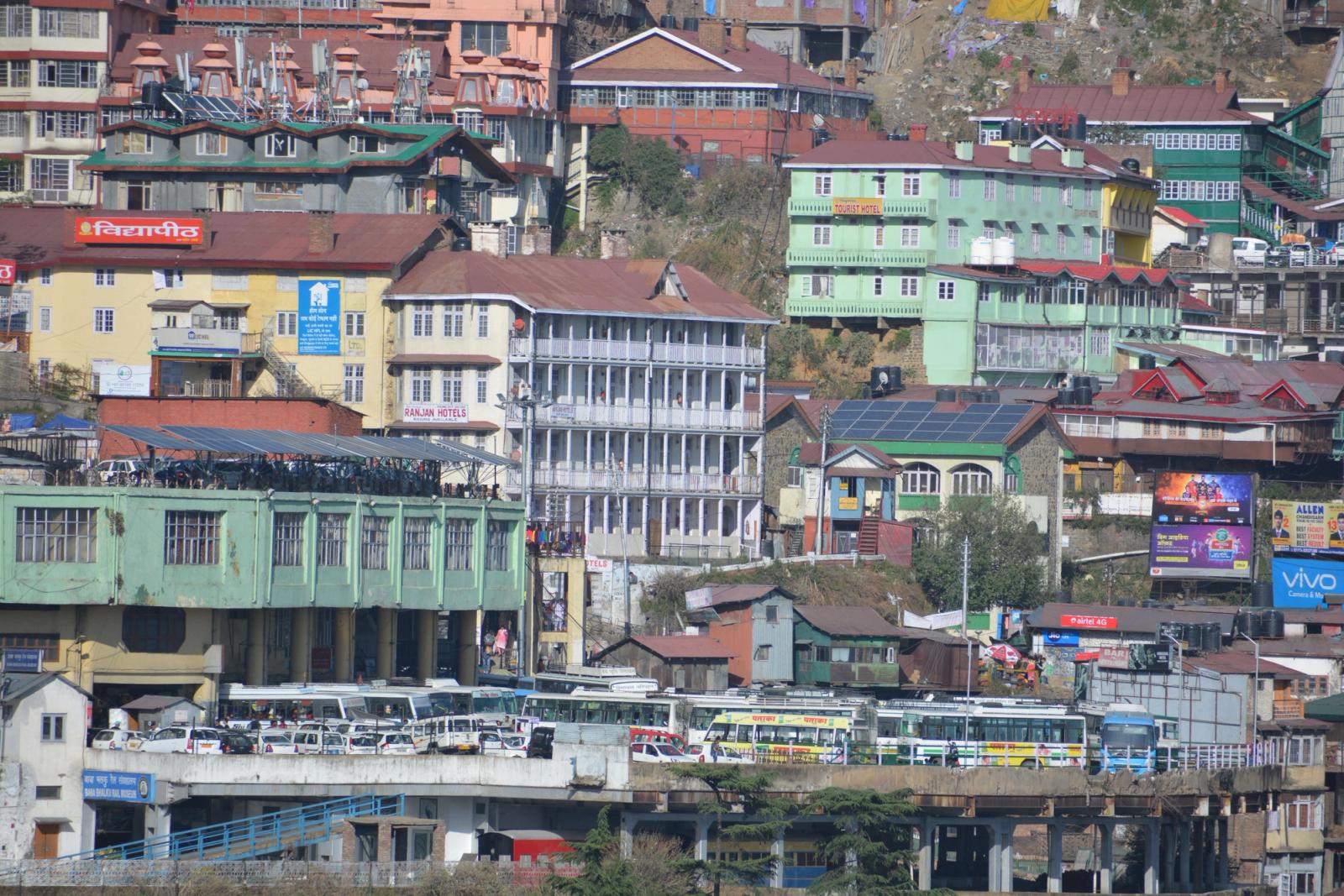 Colourful multistorey buildings clustered on a steep hillside above a bus terminal