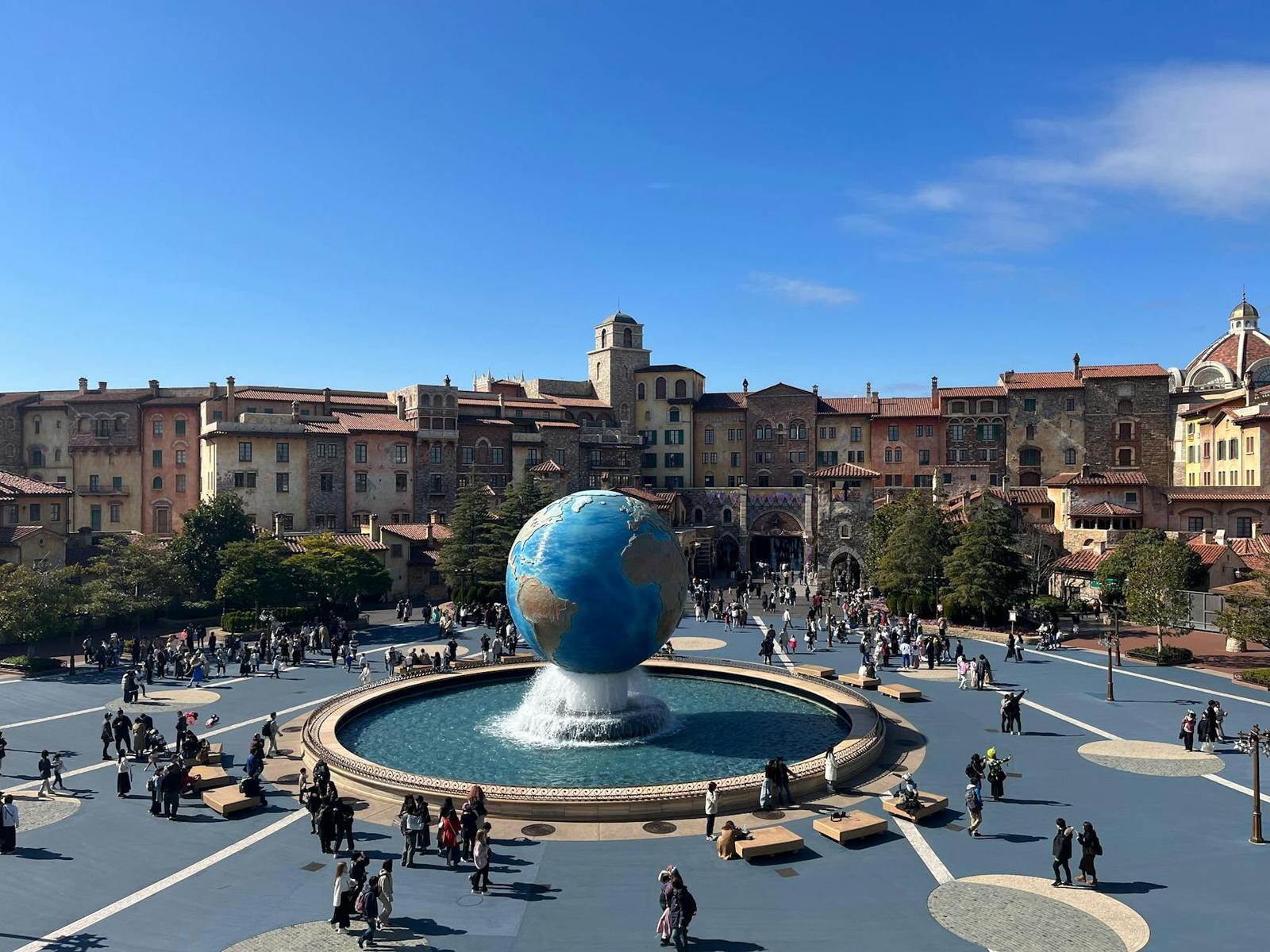 A spherical globe fountain in a plaza ringed by Mediterranean-style buildings