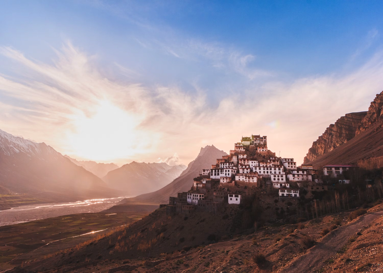 Tiered monastery buildings clinging to a hillside above a valley at sunrise