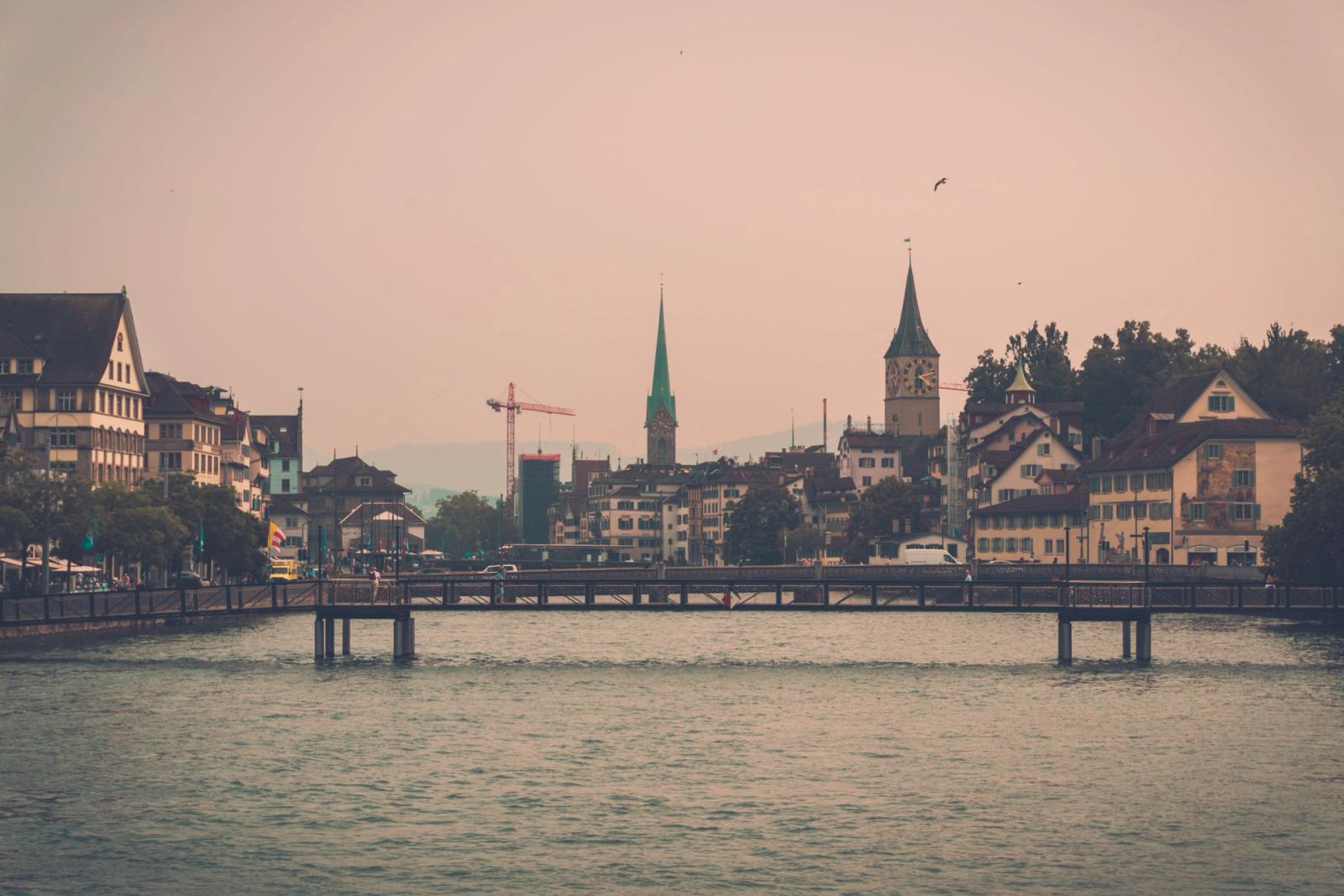 A picturesque view of Zürich's skyline with iconic church spires reflected in the calm waters at dusk