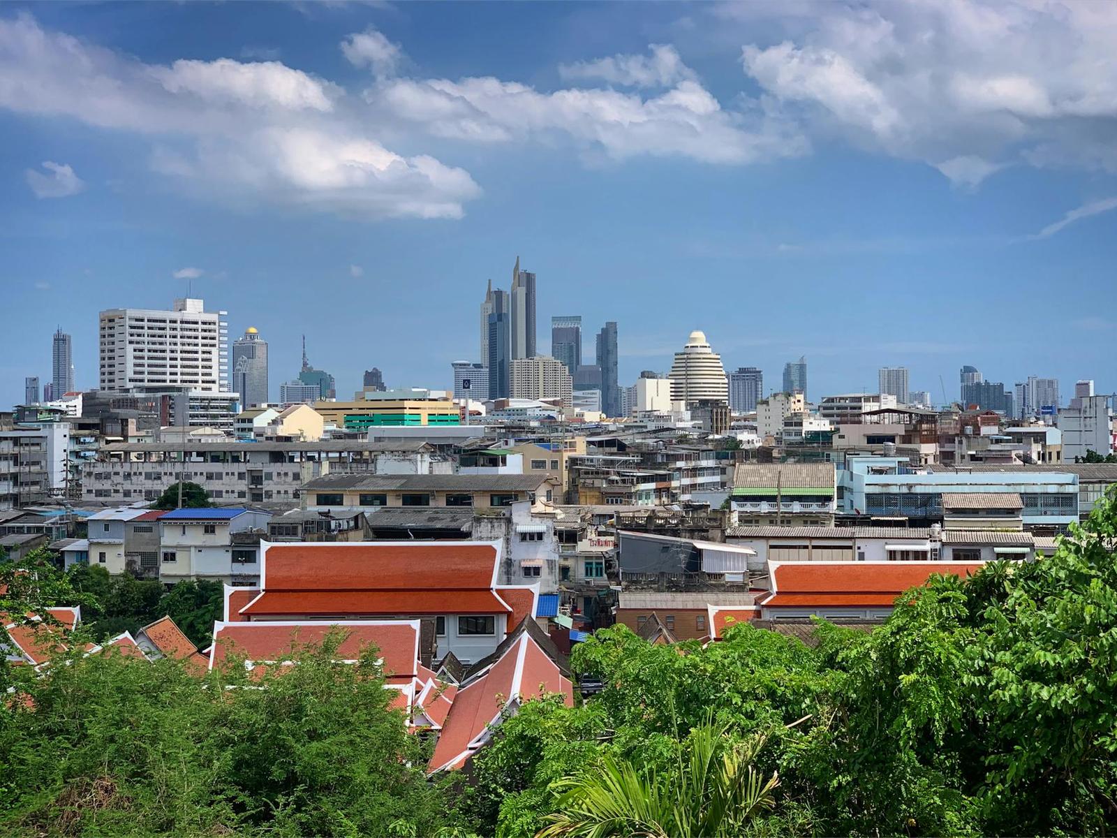 A city skyline of towers rising behind red-roofed temple buildings and greenery