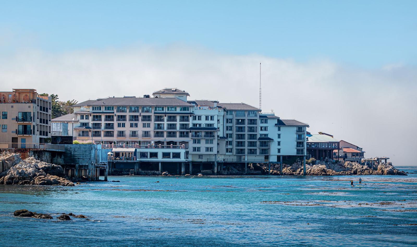 A row of waterfront hotel buildings on rocks with swimmers in the sea below