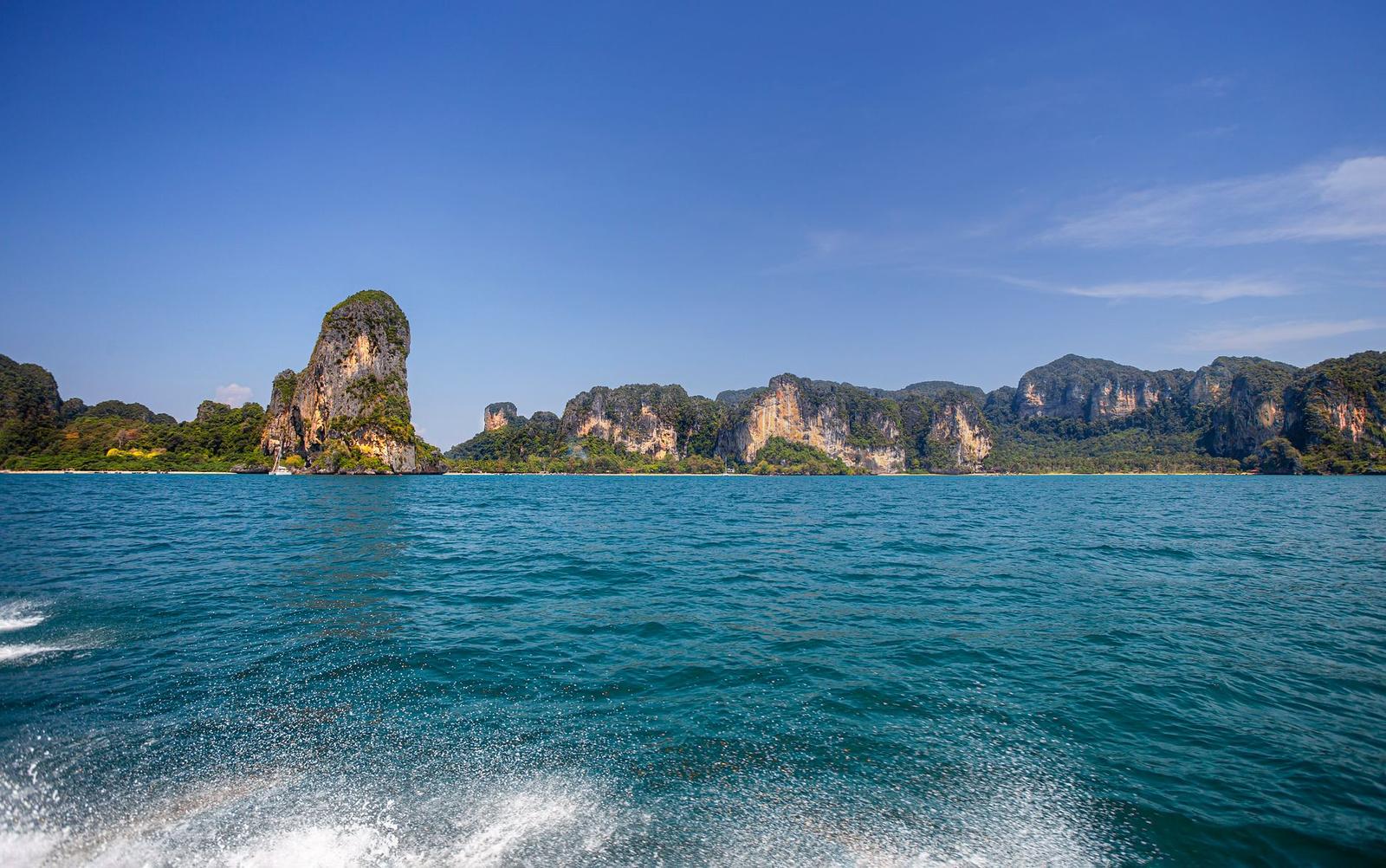 Boat wake cutting toward distant limestone cliffs at sea