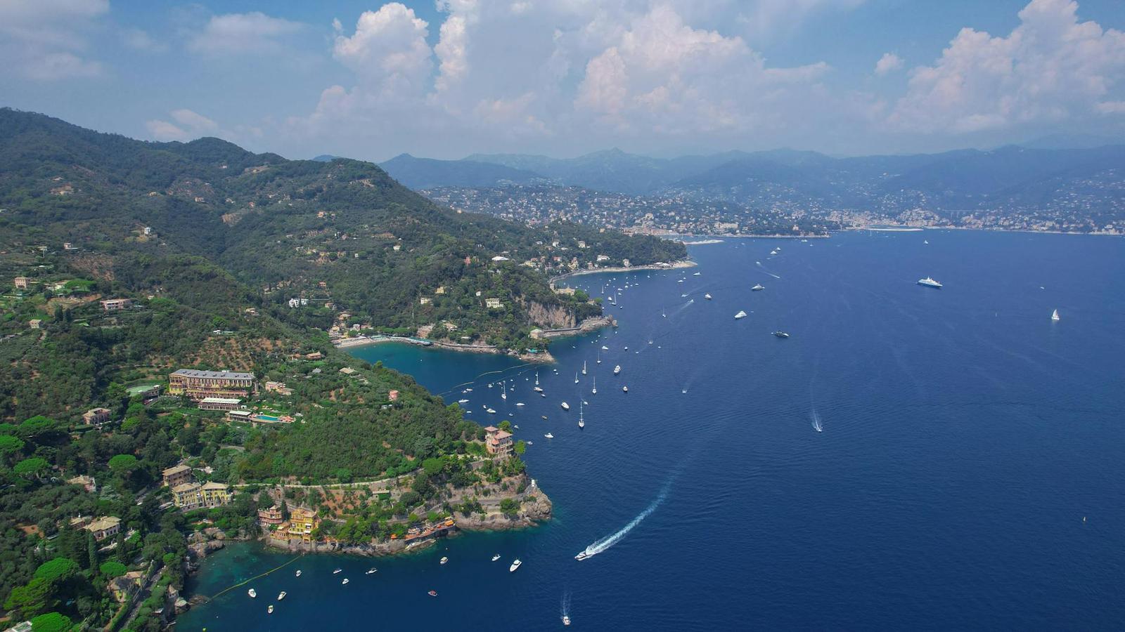 Aerial view of a wooded coastal peninsula with boats scattered across a bay