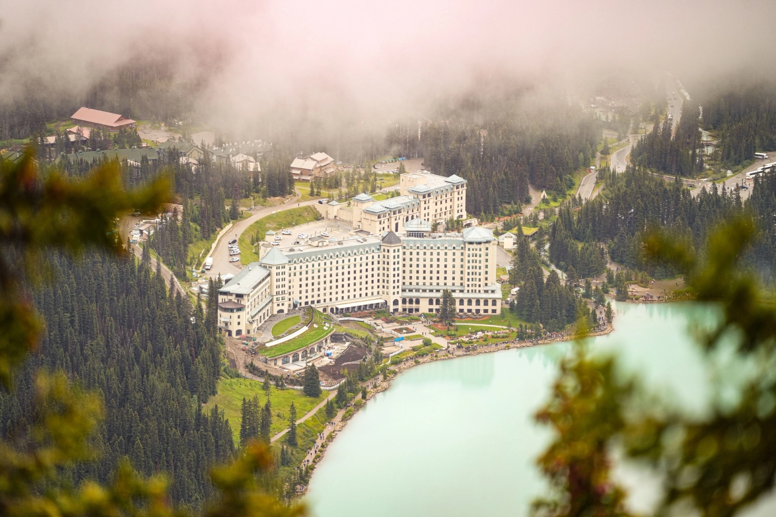 Aerial view of a grand hotel surrounded by forested mountains and turquoise lake at Lake Louise, Alberta, Canada