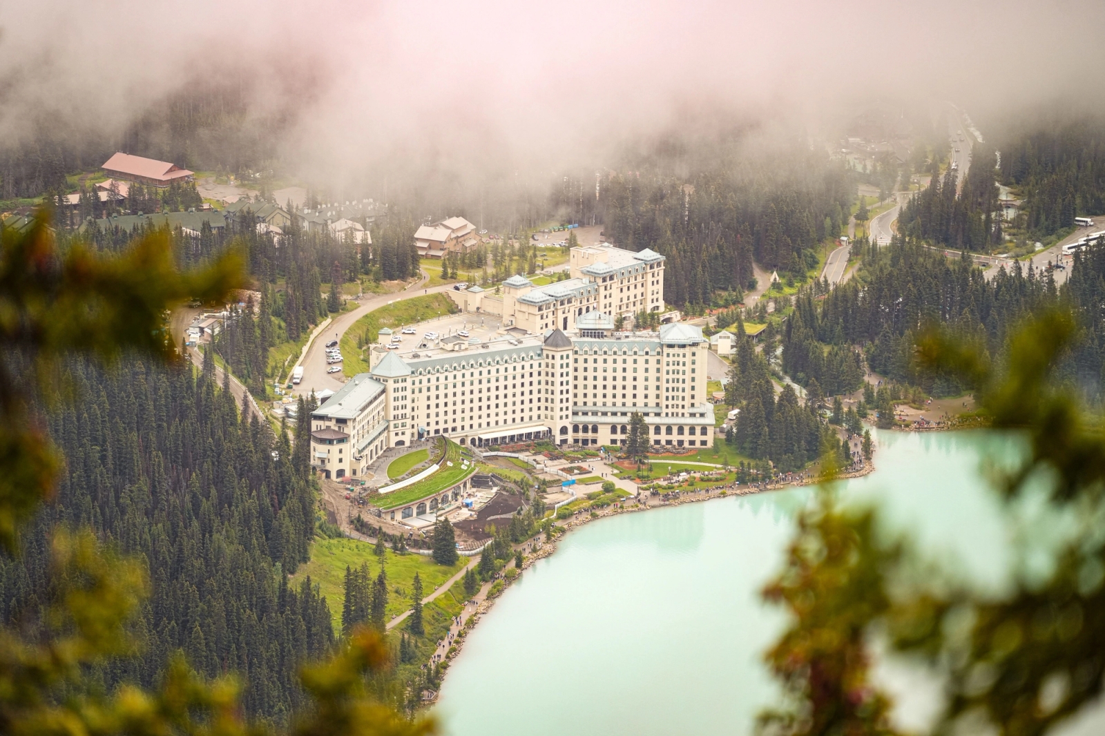 Aerial view of a grand hotel surrounded by forested mountains and turquoise lake at Lake Louise, Alberta, Canada