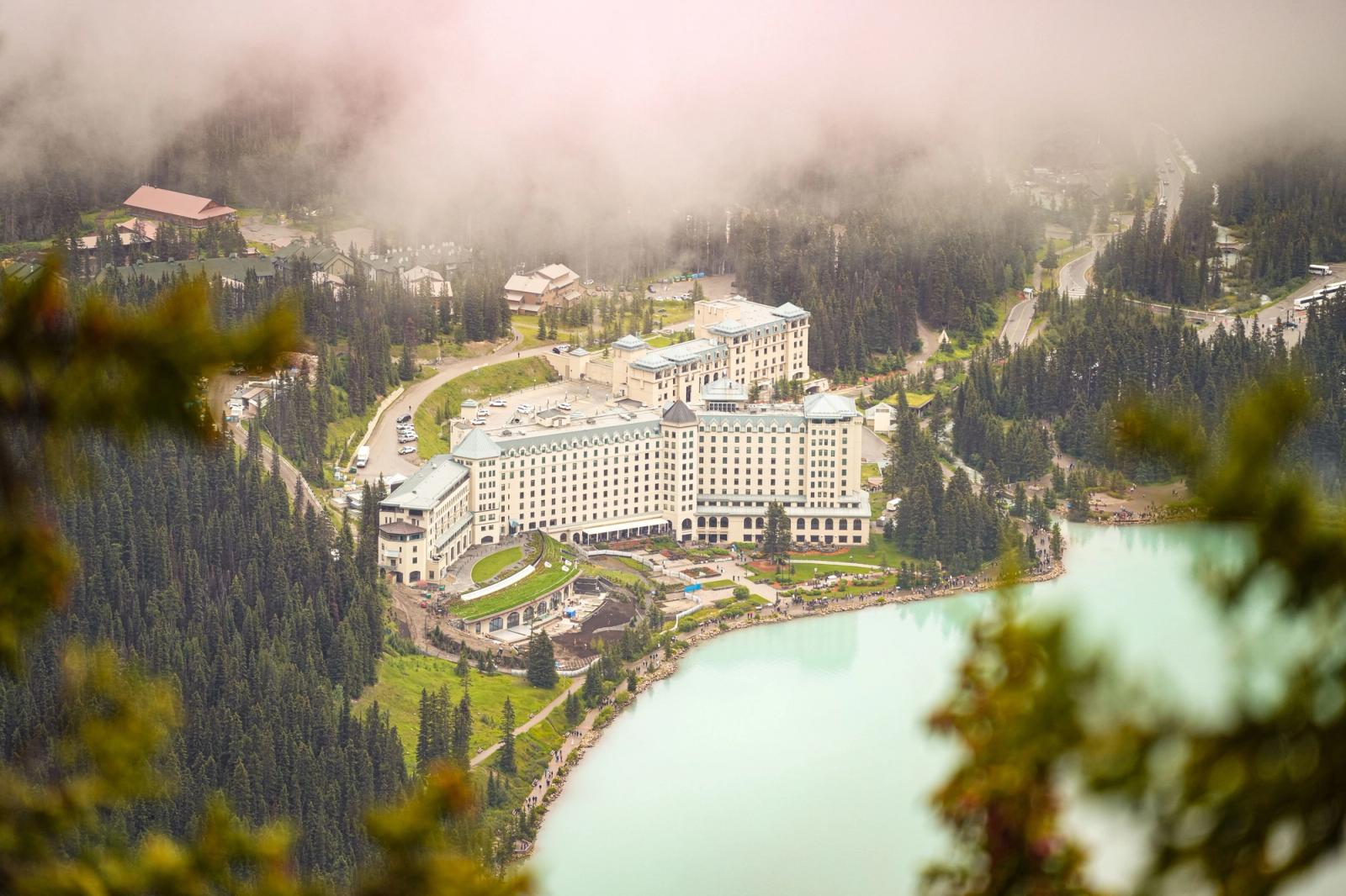 Aerial view of a grand hotel surrounded by forested mountains and turquoise lake at Lake Louise, Alberta, Canada