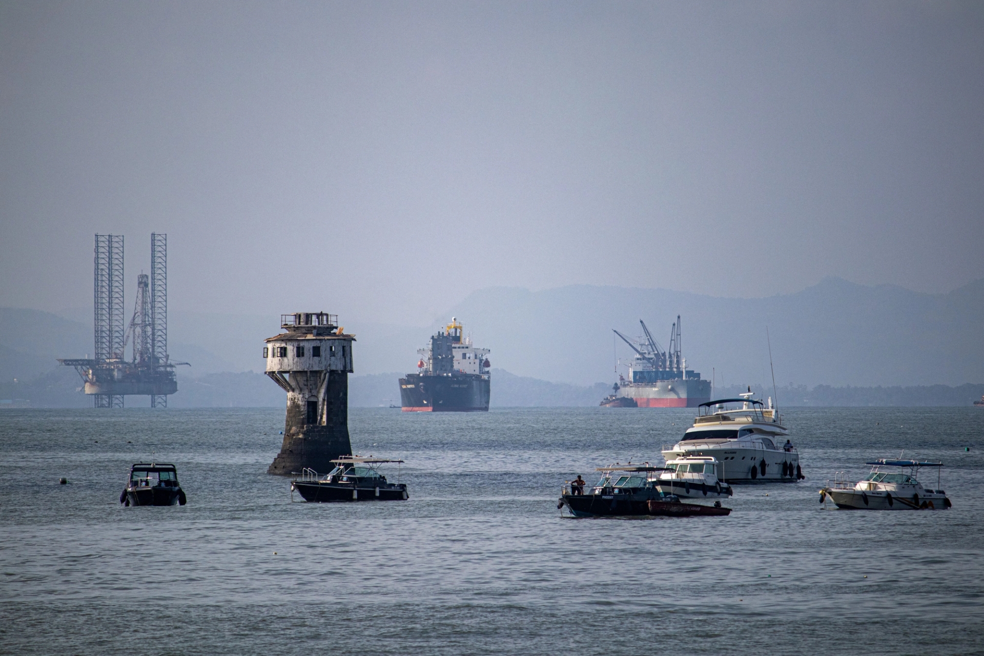 A scenic view of various ships and a tower in Mumbai harbor, India, with an oil rig in the background